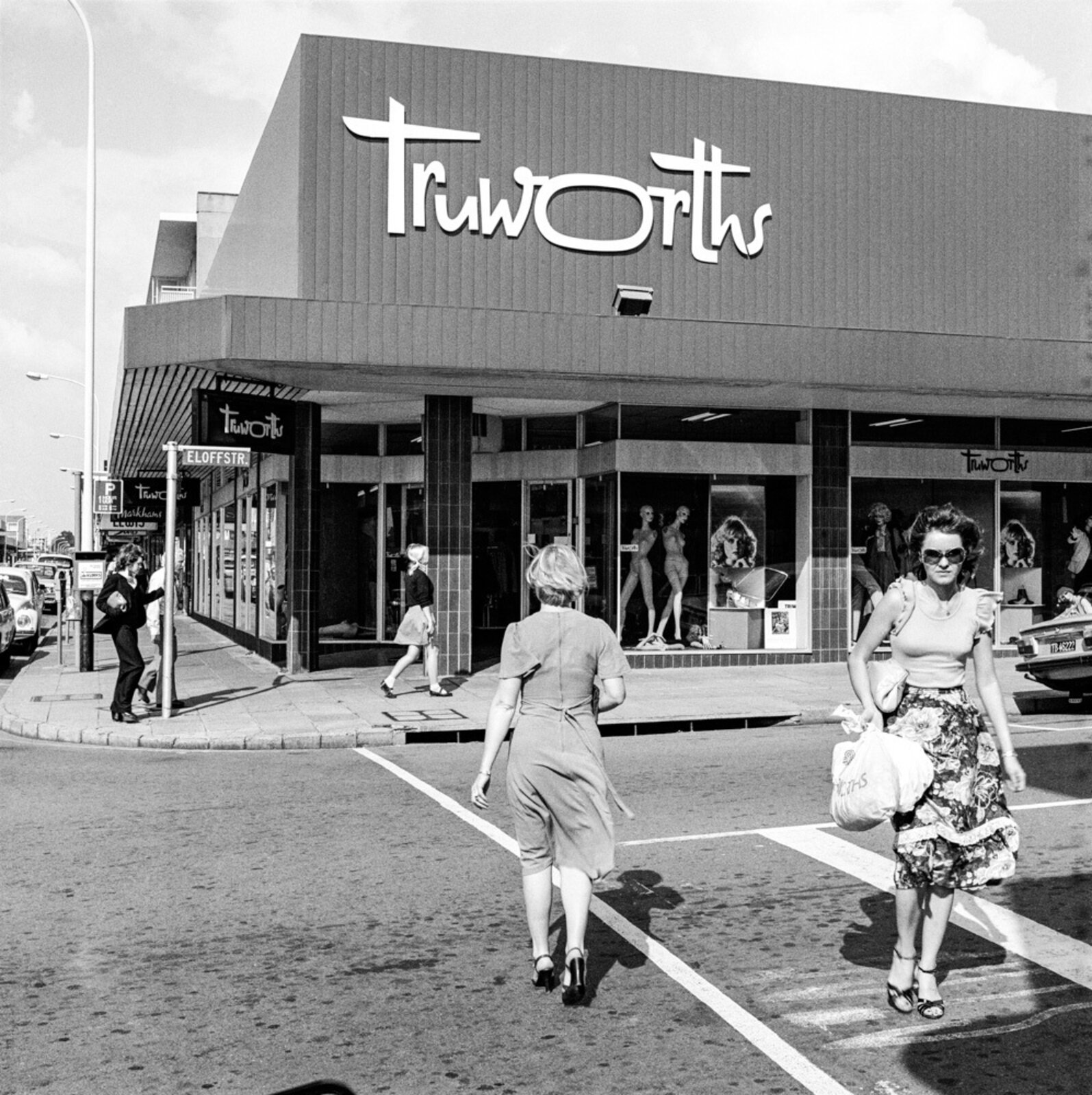 A black and white photo of two women walking in front of a store.