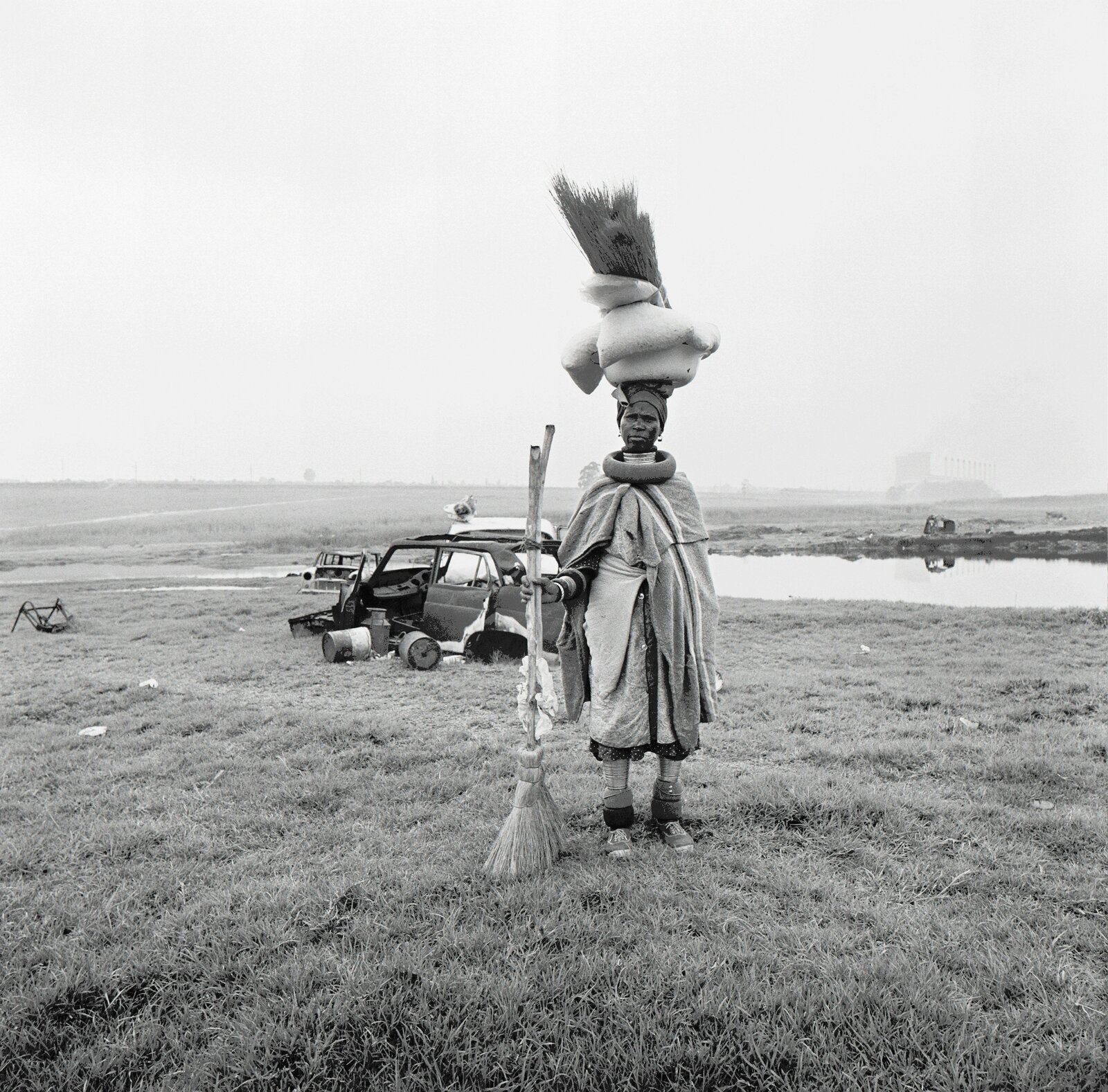 A black and white photo of a woman with a broom in a field.