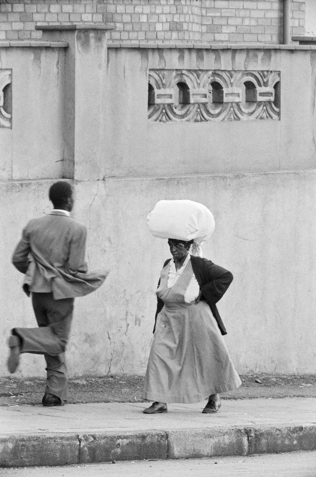 Anna Lebako, a washerwoman from Soweto carrying the week's laundry to a white suburban family, Harrow Road by David Goldblatt, 1961