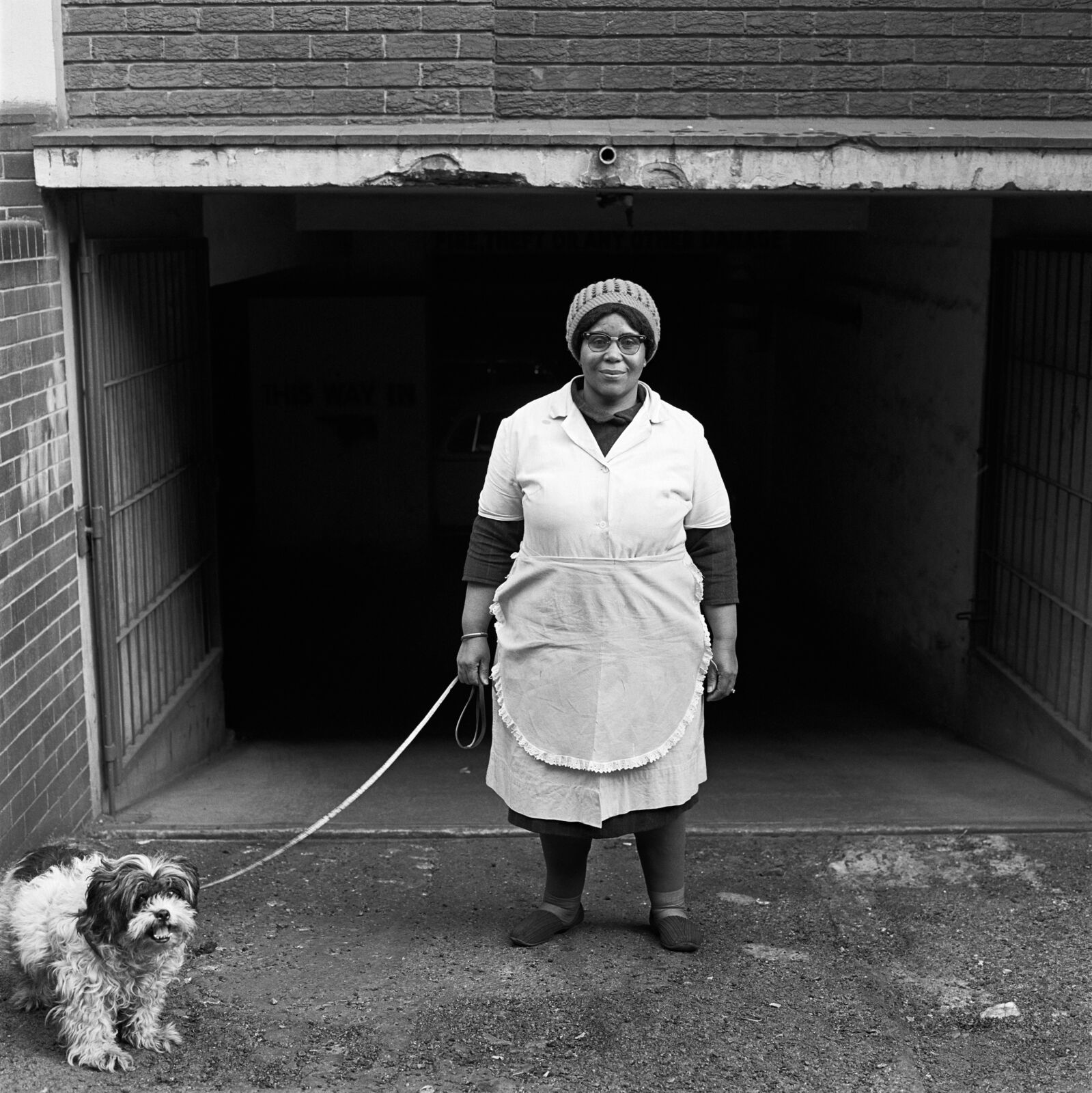 A woman standing in front of a garage with a dog on a leash.
