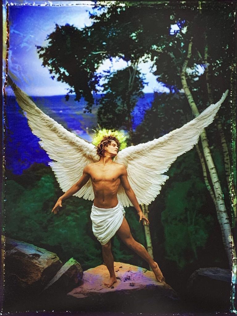 A painting of an angel standing on a rock in the woods.