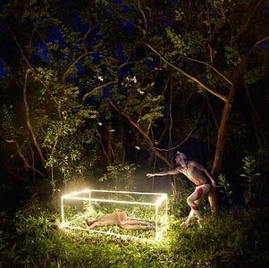 a man standing next to a woman laying on the ground in the woods
