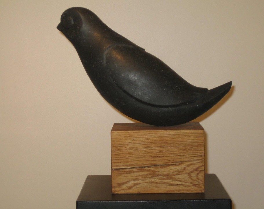 A black bird sitting on top of a wooden block.