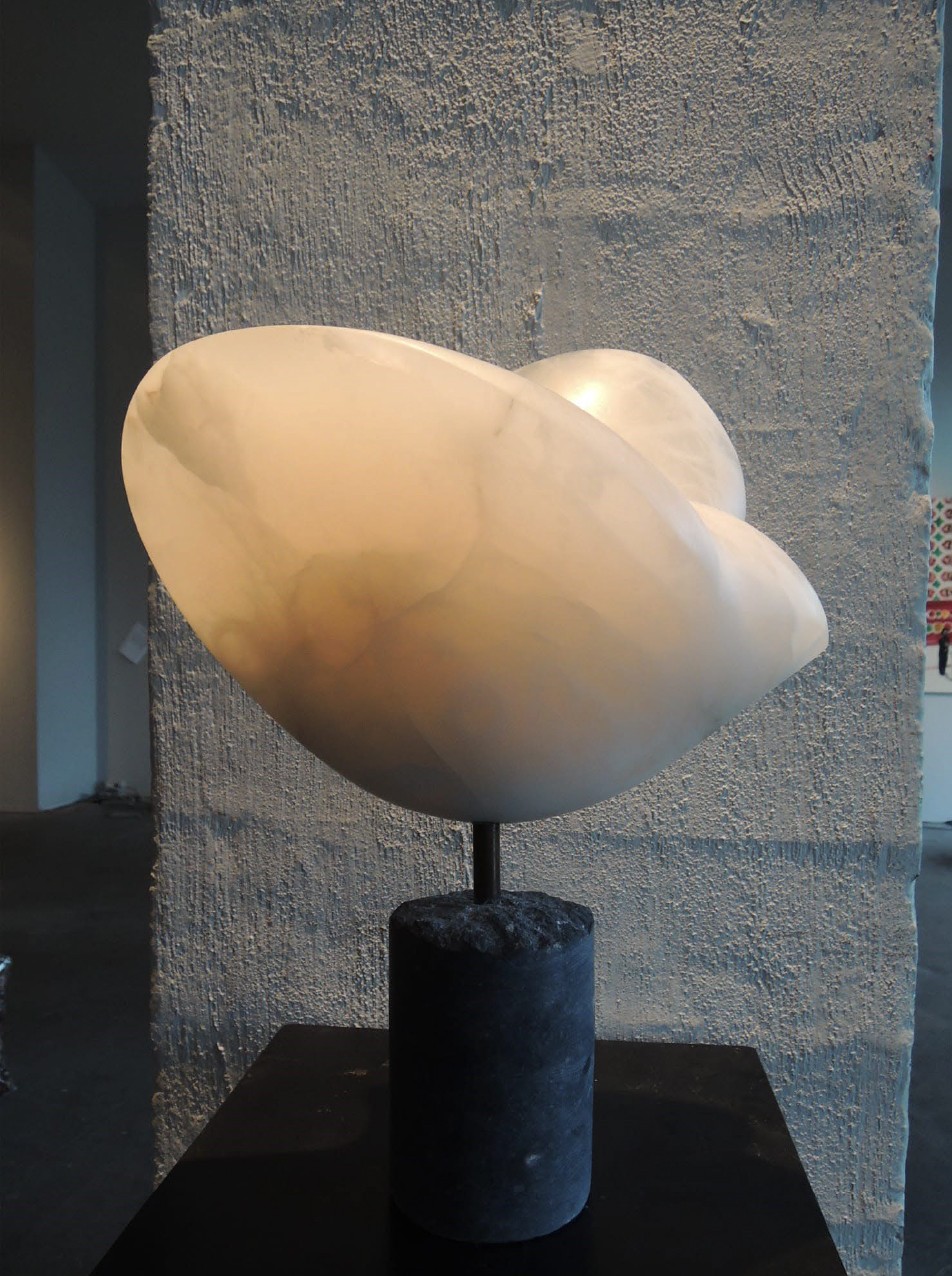 A sculpture on a black pedestal in front of a wall.