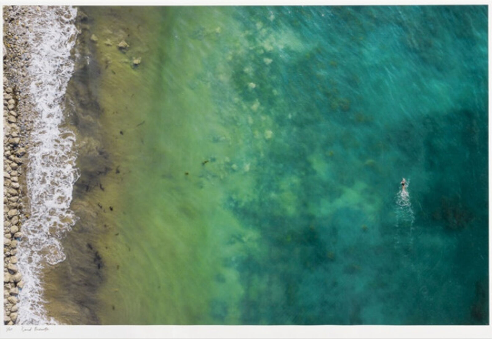 A person swimming in the ocean near a rocky beach.