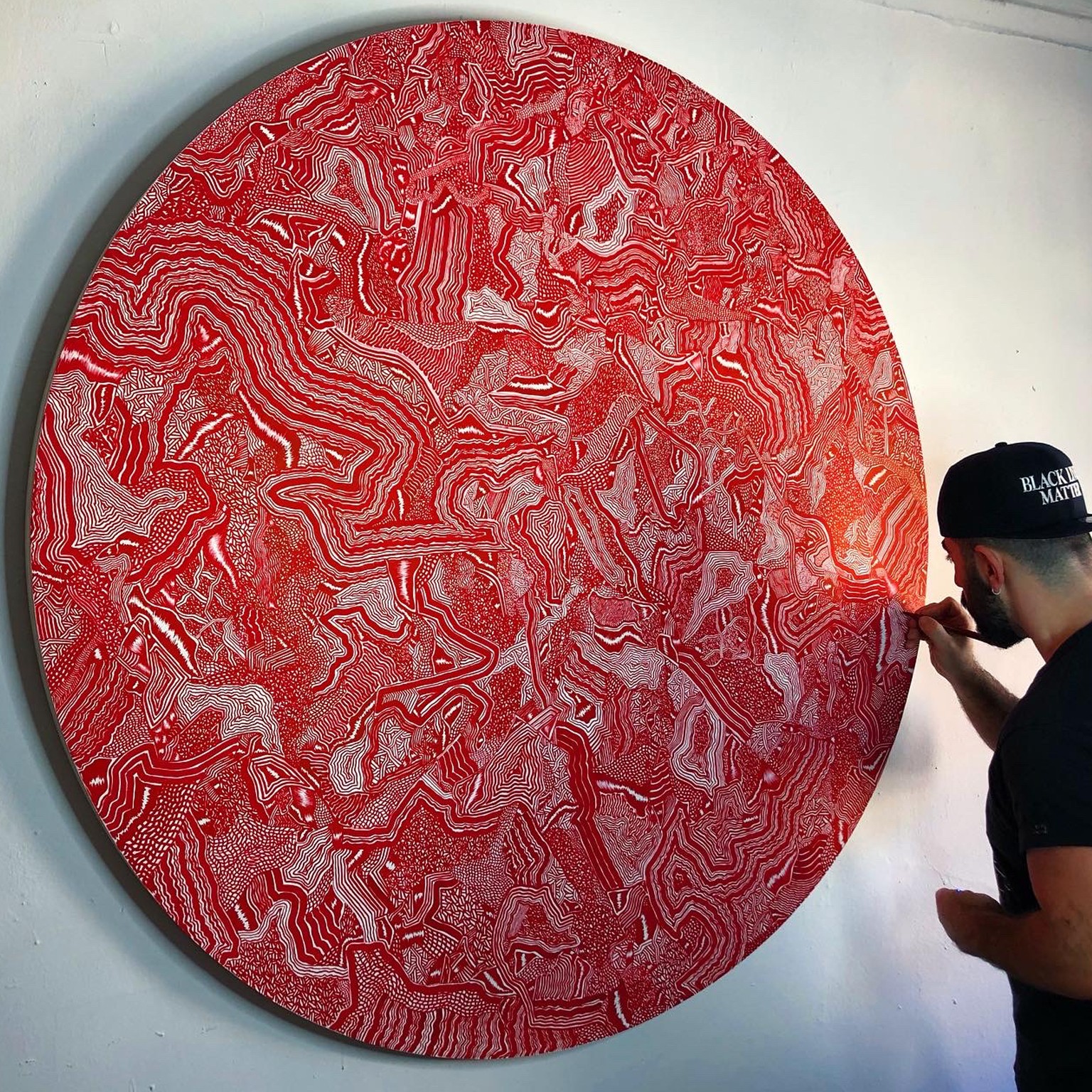 A man is painting a large red circle on a wall.