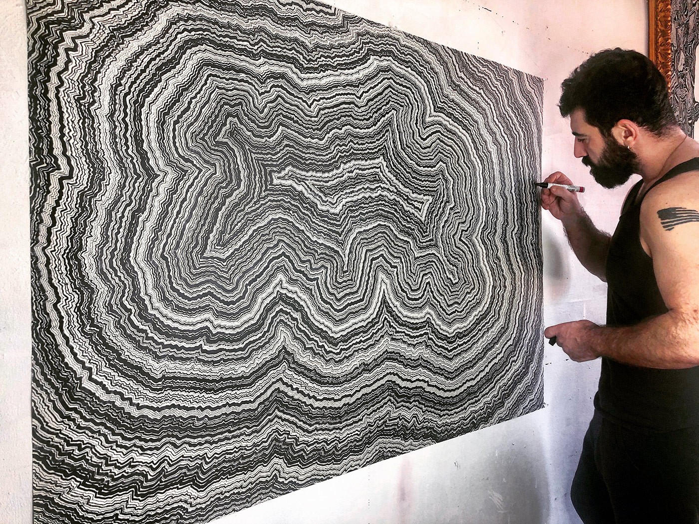 A man is painting a large black and white drawing on a wall.