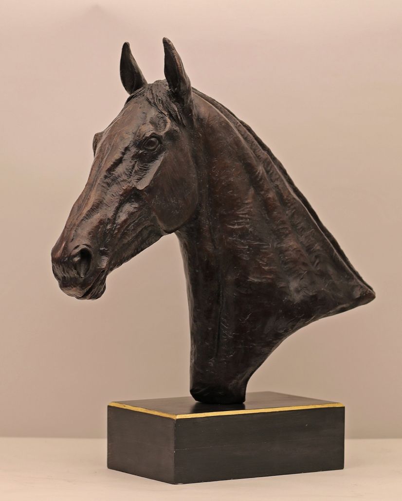 A bronze sculpture of a horse head on a wooden base.