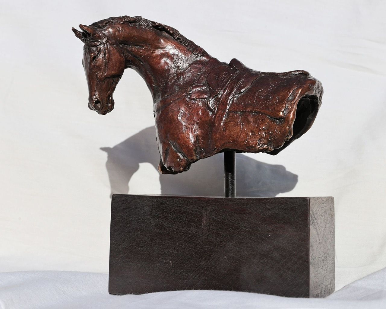 A bronze sculpture of a horse head on a wooden base.
