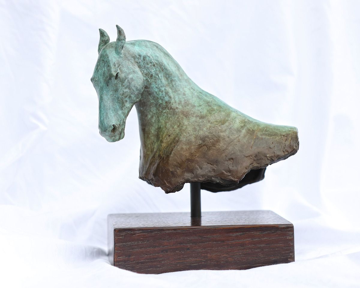 A bronze sculpture of a horse head on a wooden base.
