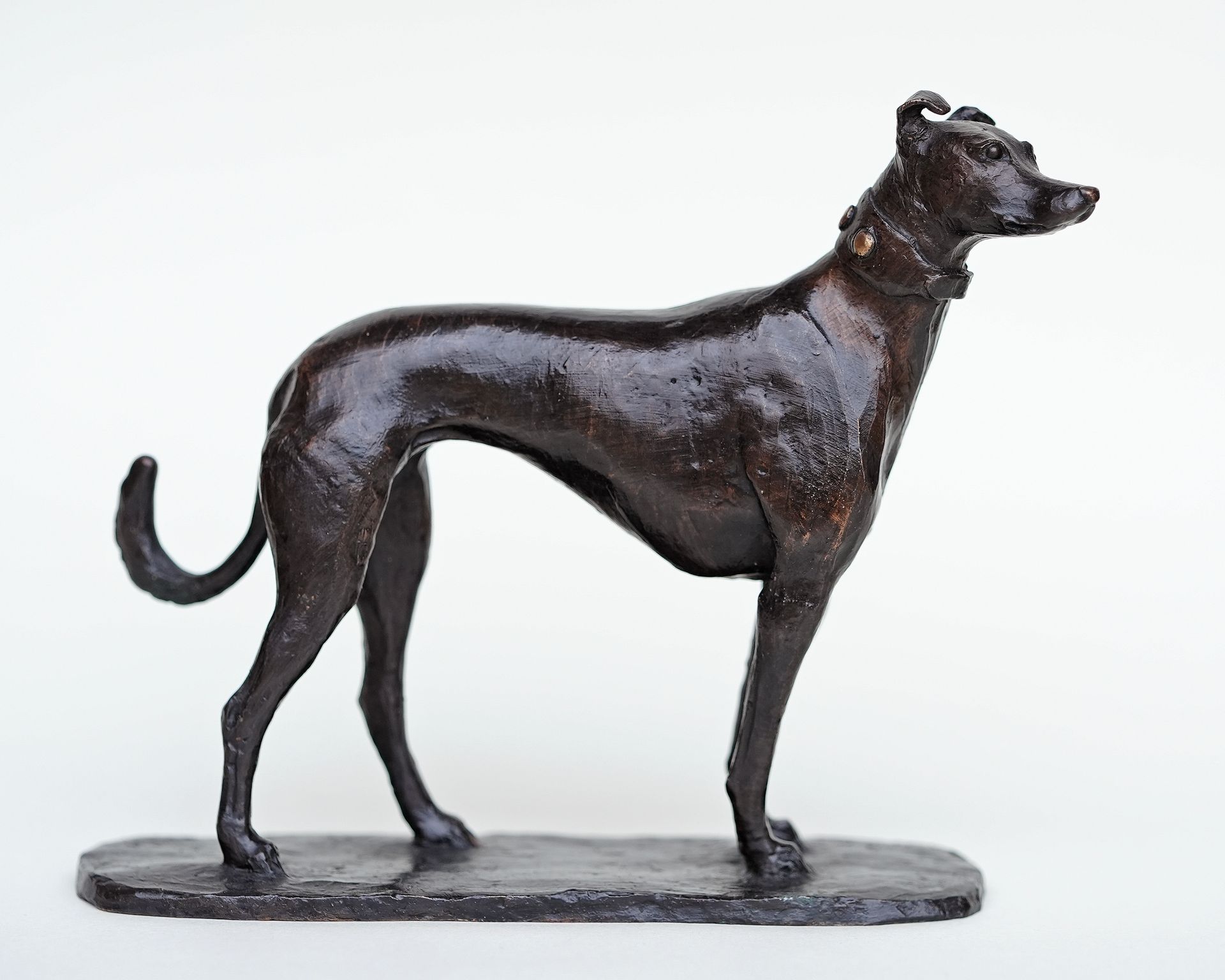 A bronze statue of a greyhound standing on a white background.