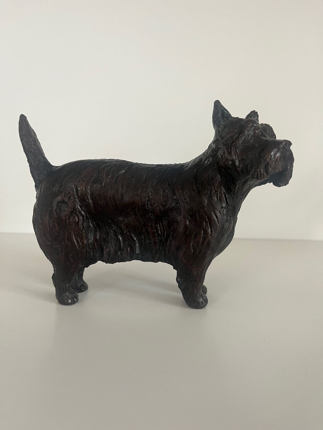 A dark, textured sculpture of a small dog standing on a white surface.