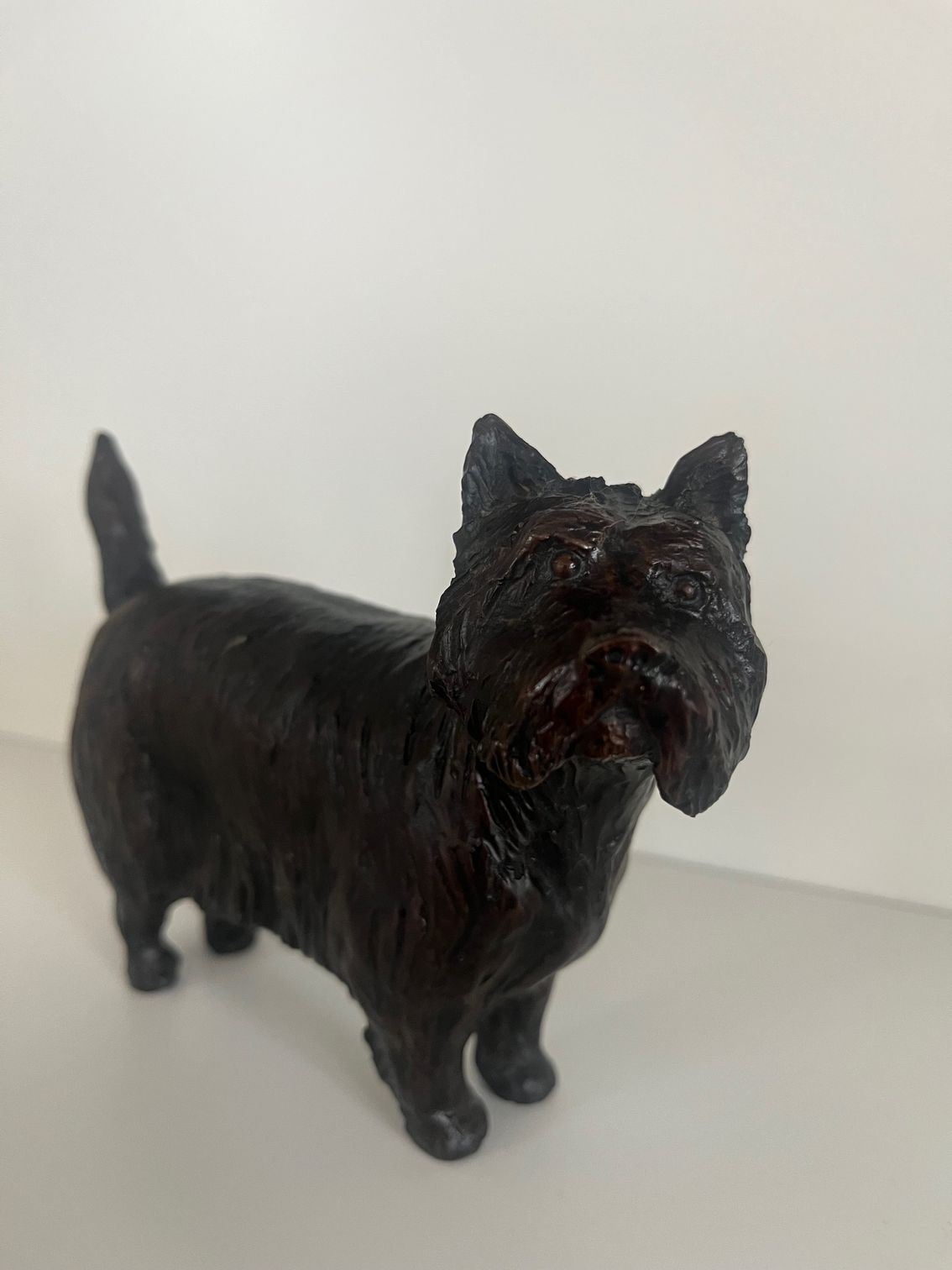 A dark, textured sculpture of a small dog standing on a white surface.