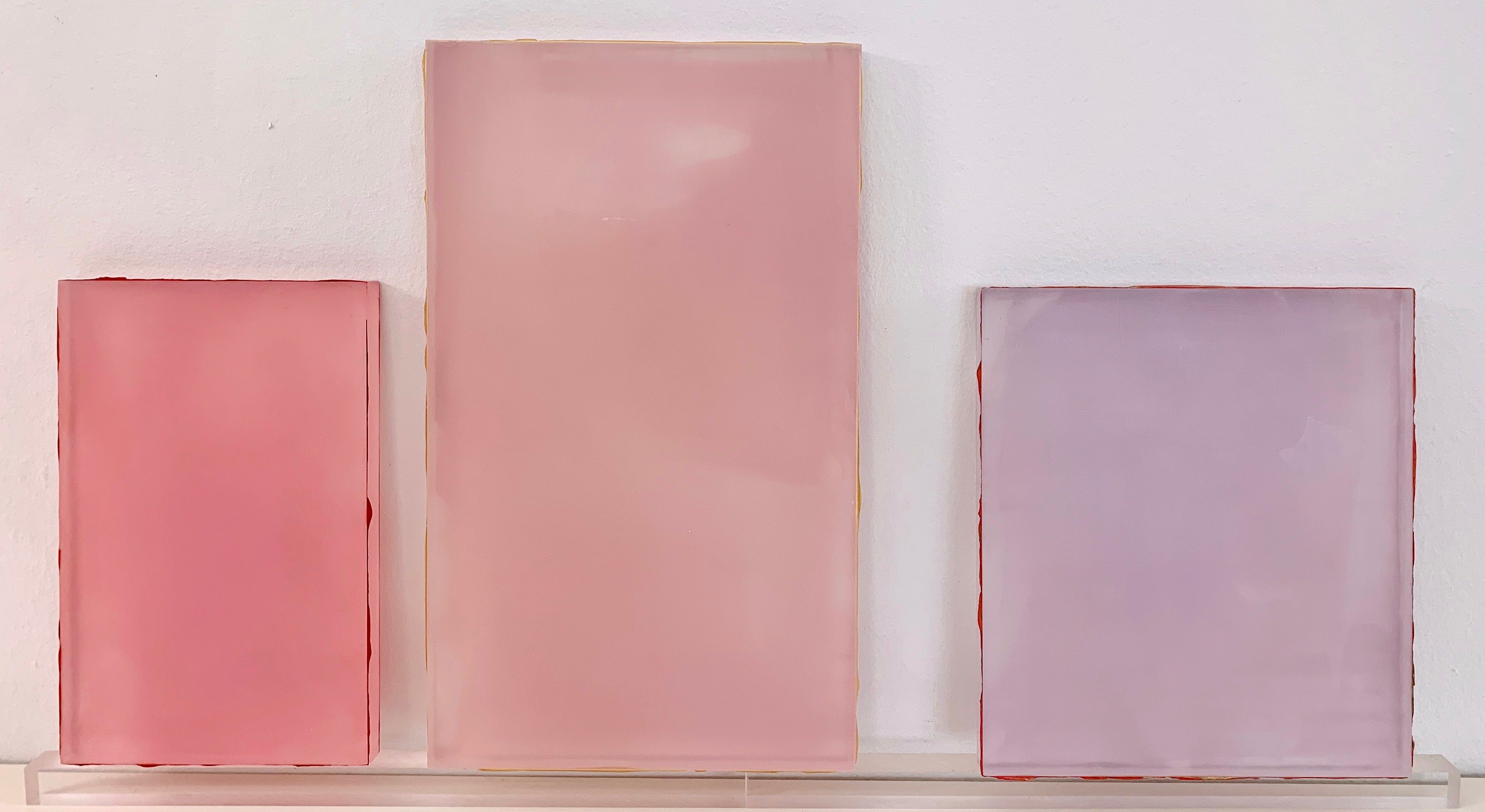 Three pink and purple glass panels on a white wall.