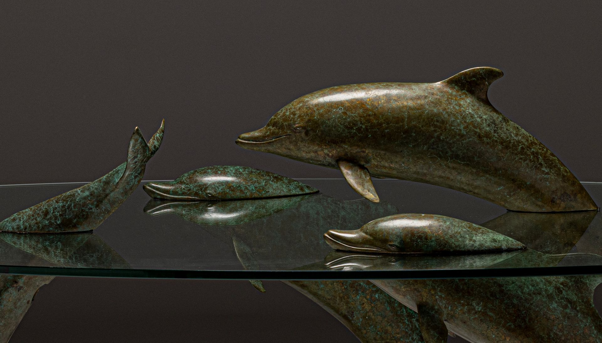 A sculptural coffee table featuring bronze dolphin figures supporting a glass top.