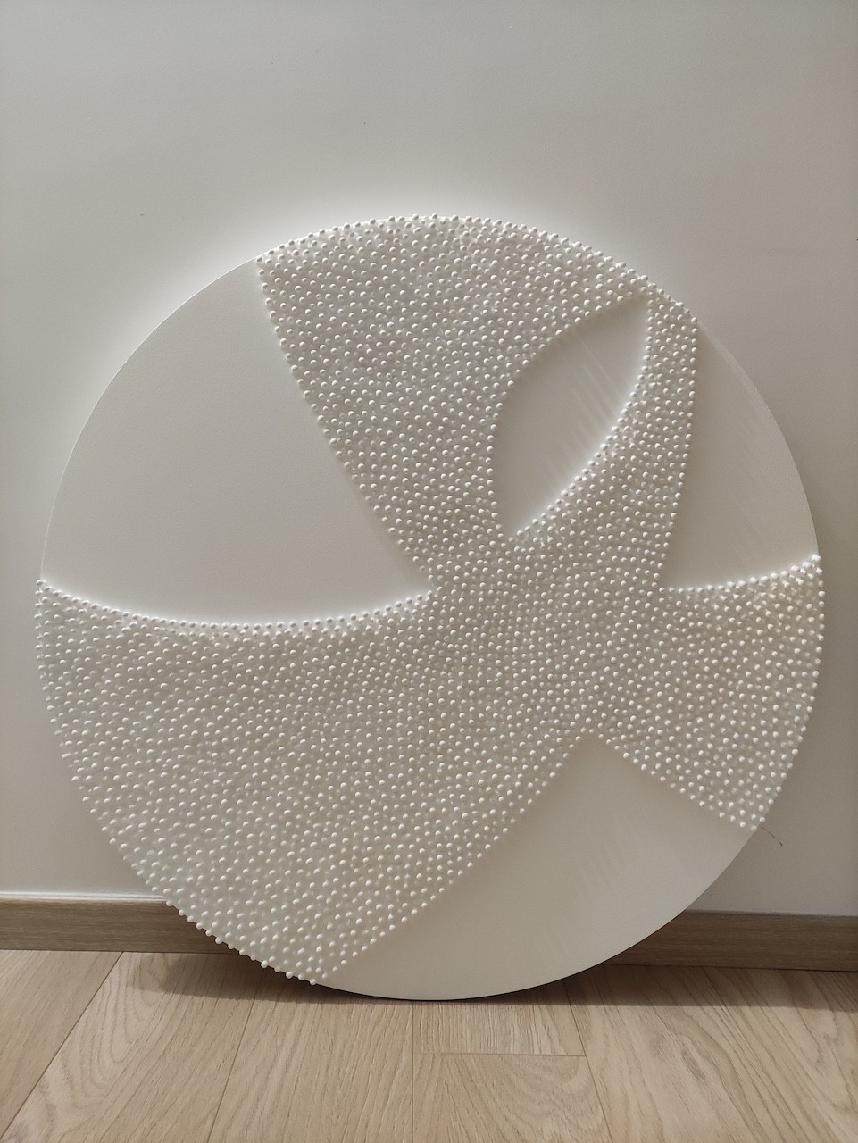 A large white sculpture on a wooden floor next to a white wall.