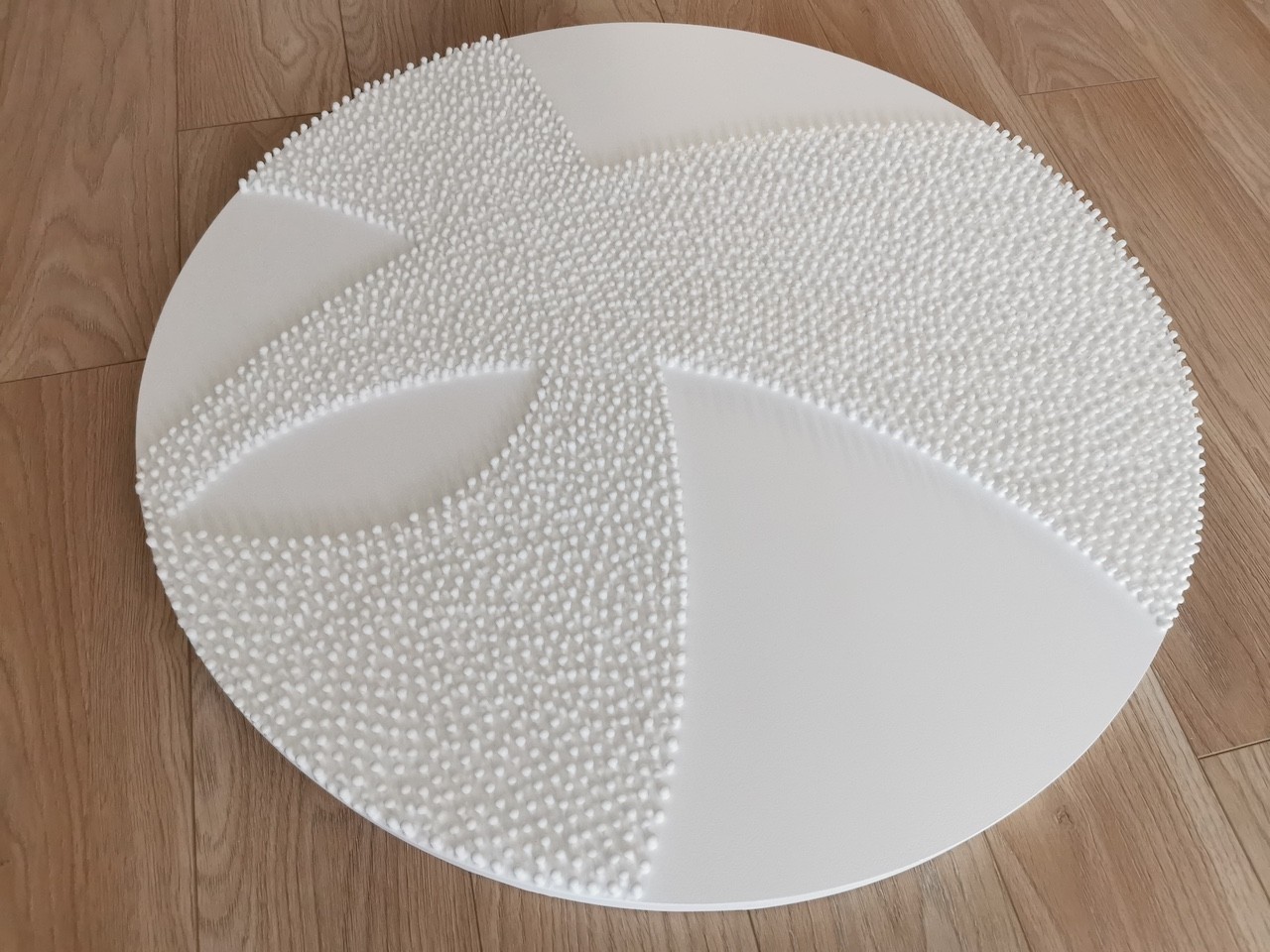 A large white sculpture on a wooden floor next to a white wall.