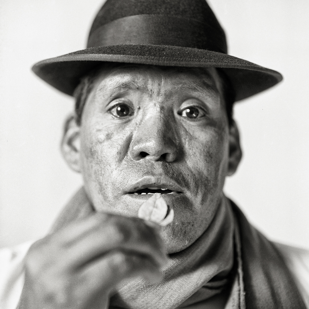 A man in a hat and scarf holding a cigarette in his mouth.