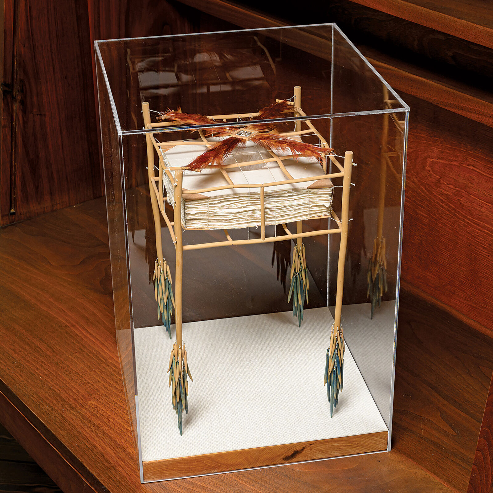 A sculptural installation featuring a woven basket suspended from a bamboo frame with feathered elements.