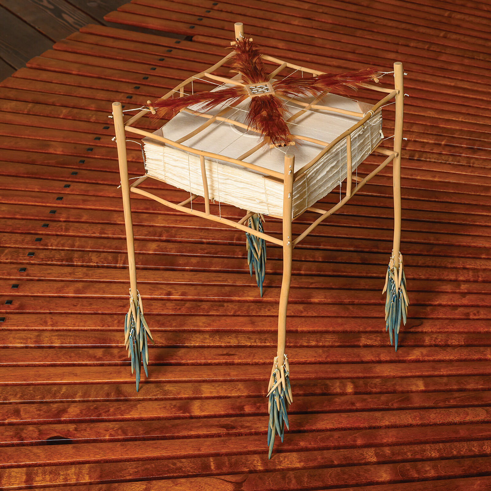 A sculptural installation featuring a woven basket suspended from a bamboo frame with feathered elements.