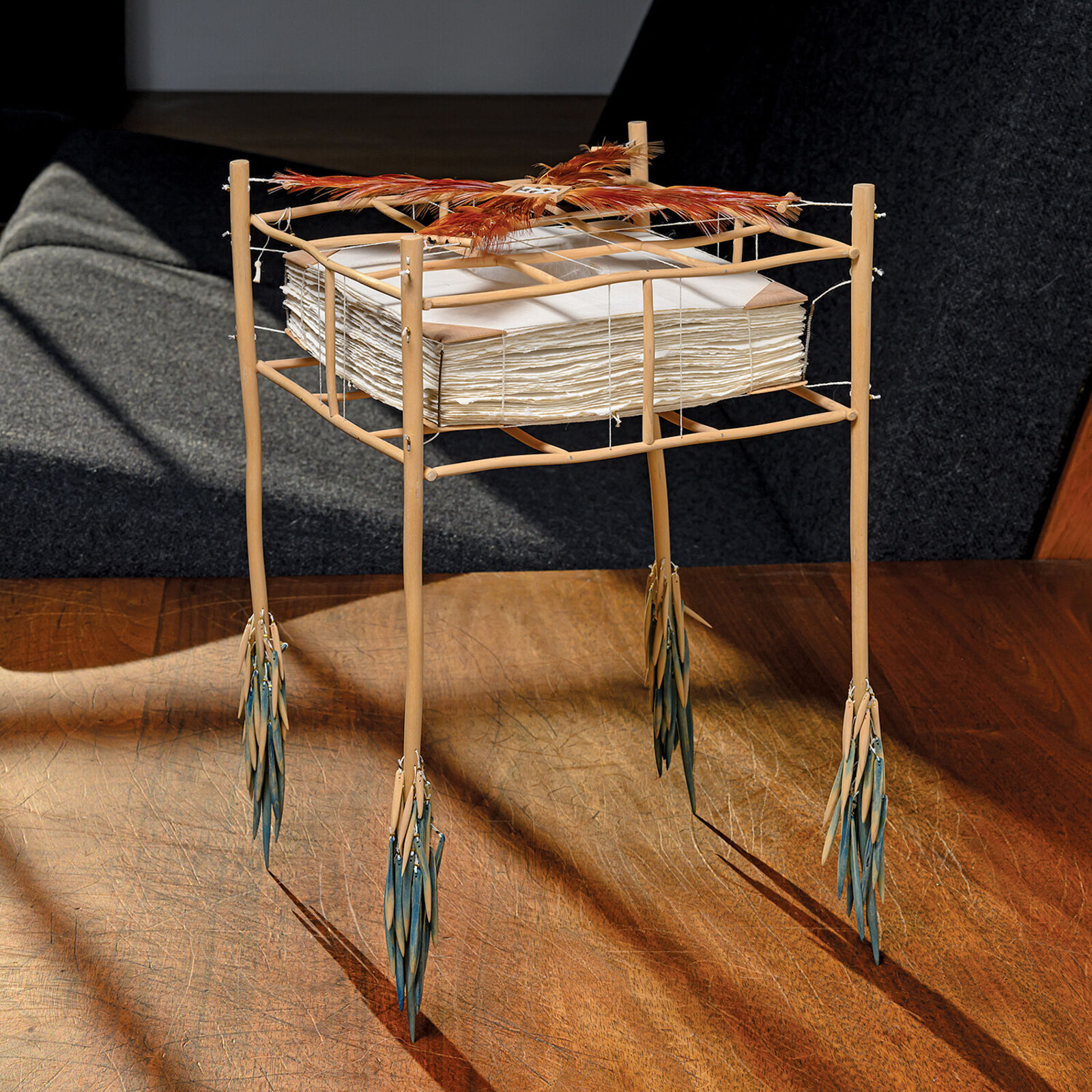 A sculptural installation featuring a woven basket suspended from a bamboo frame with feathered elements.