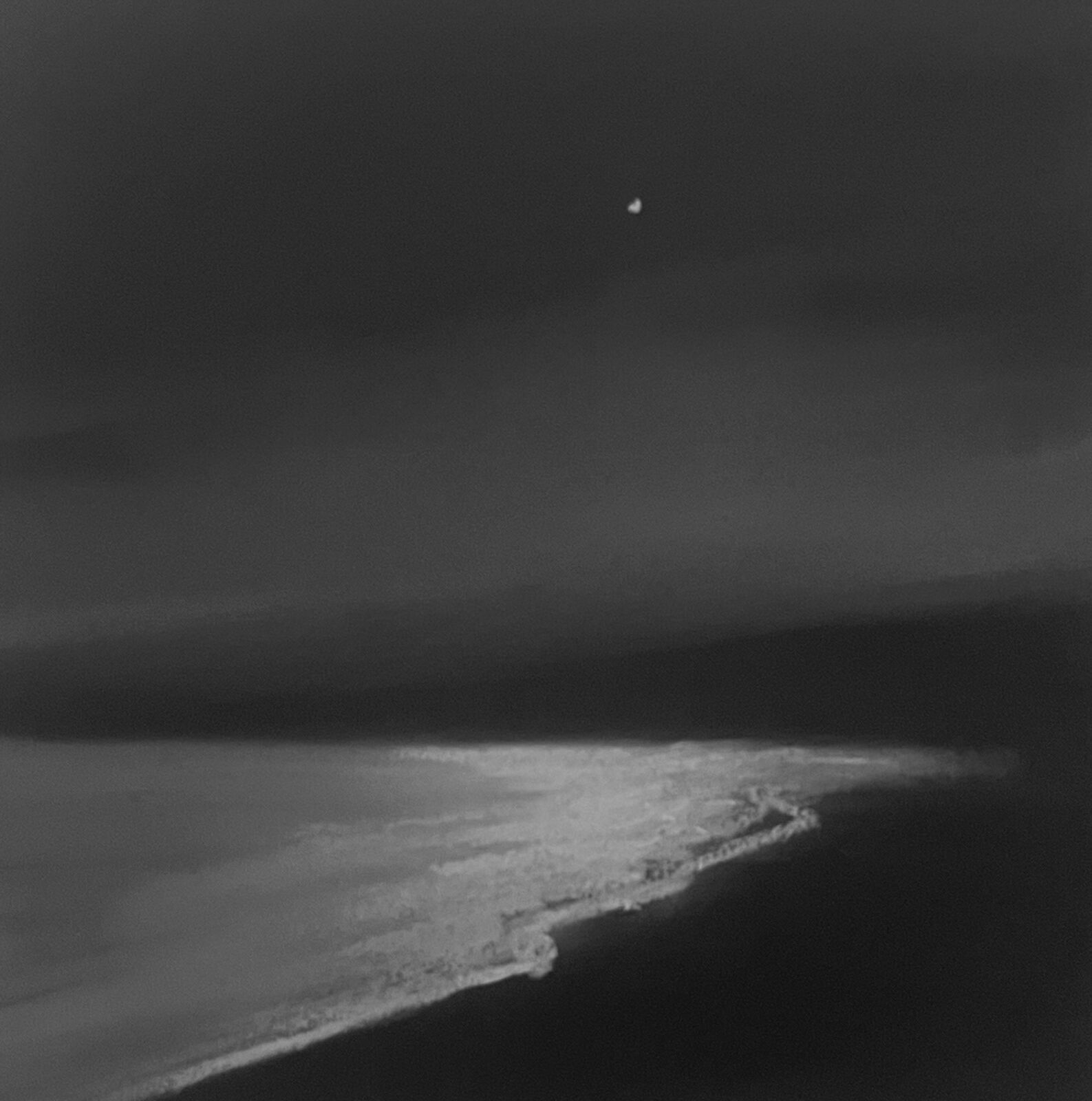 A monochrome seascape capturing the moonlit reflection on a dark shoreline.