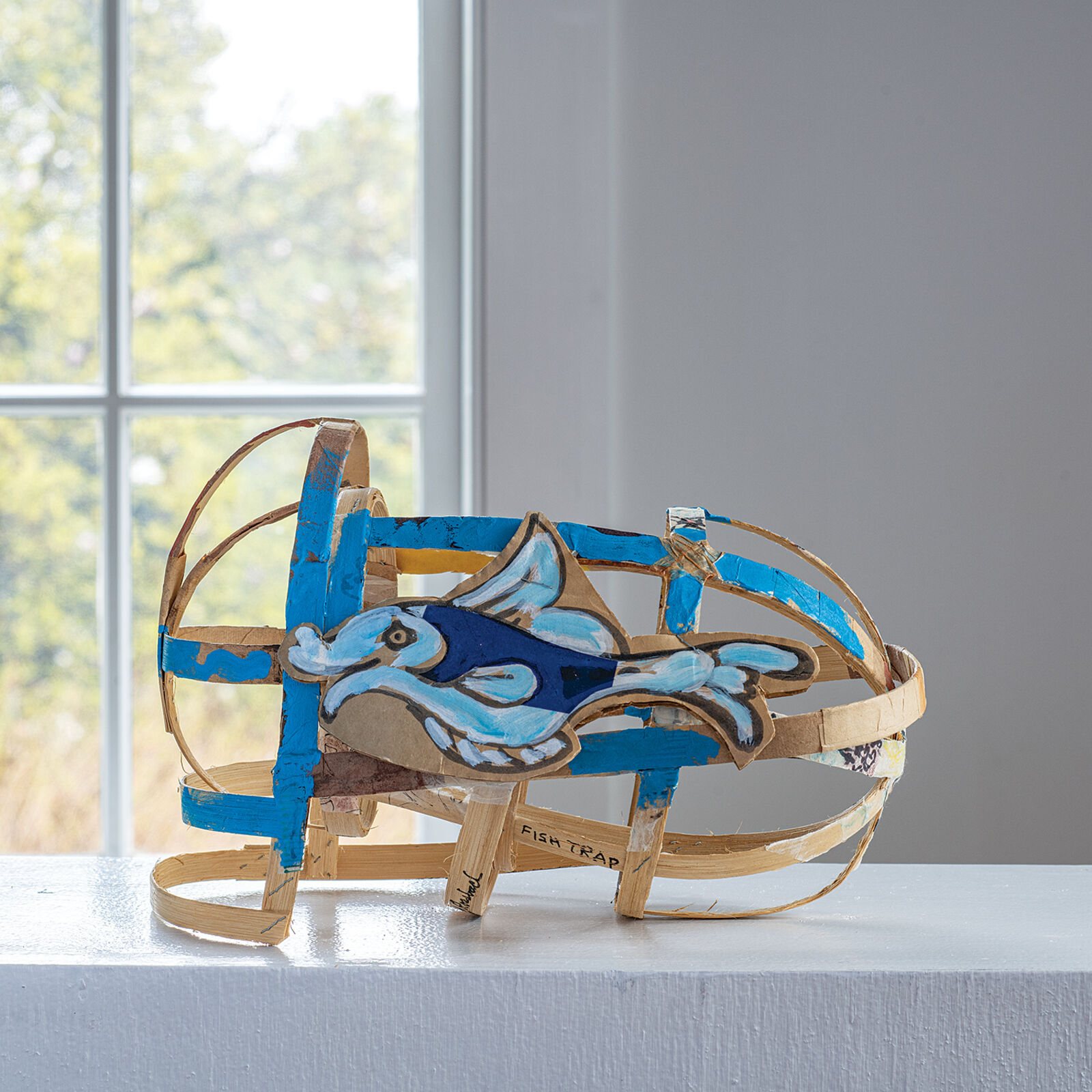 "A whimsical sculpture of a fish-shaped basket with blue and natural wood tones."
