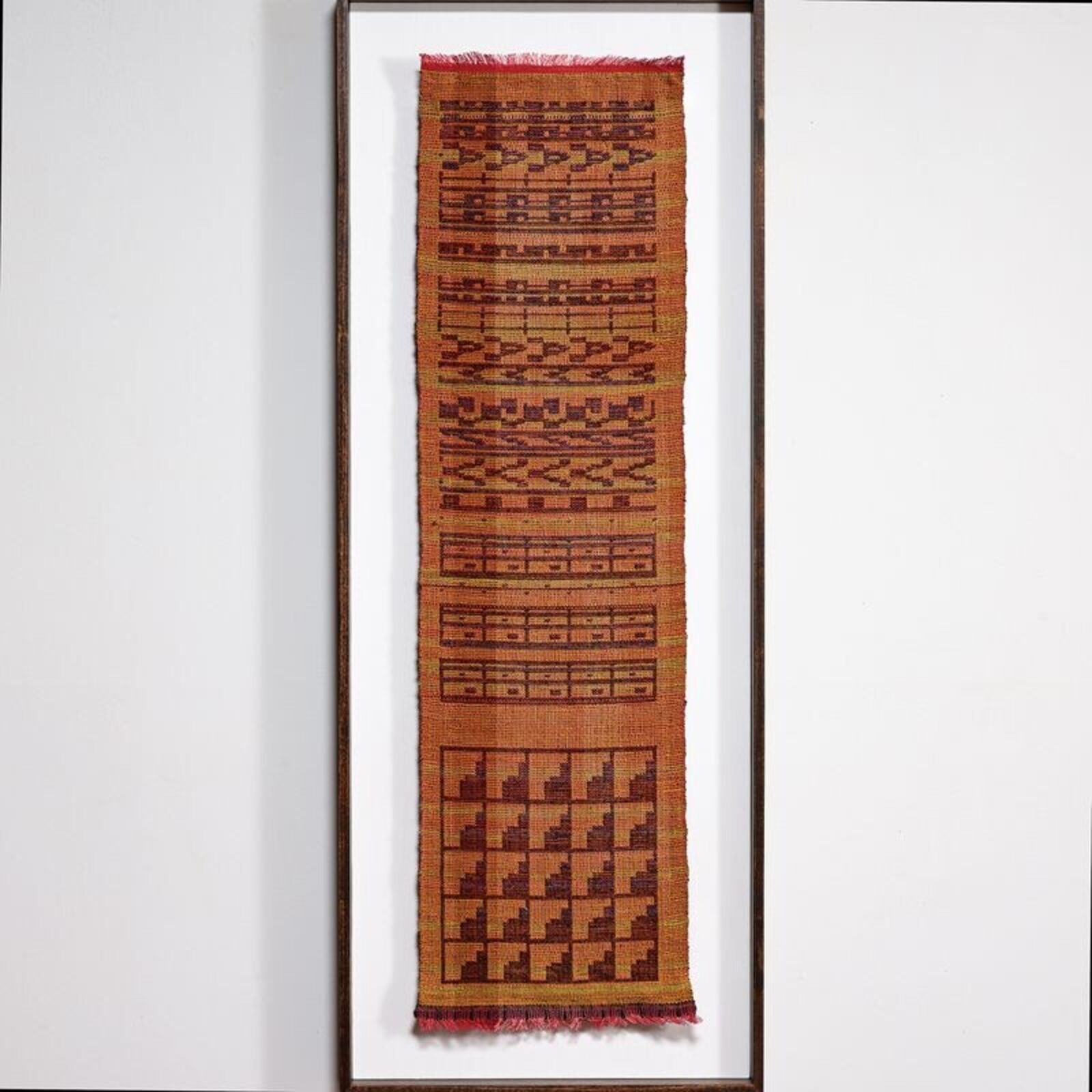A framed woven textile featuring geometric patterns in earthy tones.
