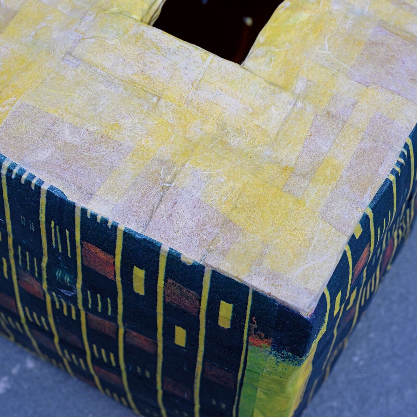 A colorful, cube-shaped box with a geometric pattern and a square opening on top.