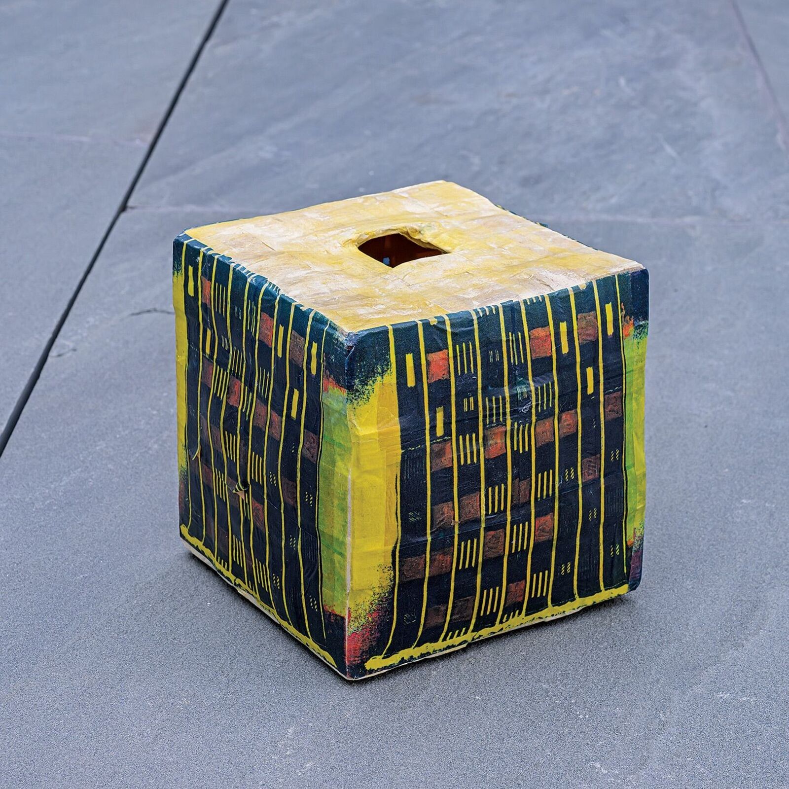 A colorful, cube-shaped box with a geometric pattern and a square opening on top.