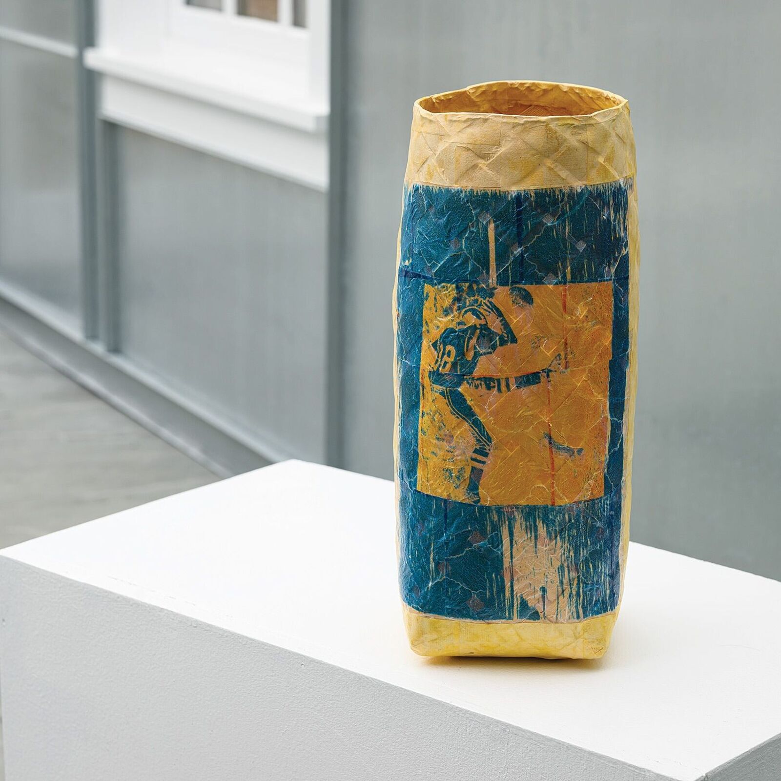 A textured, multi-colored vase featuring a blue square print of a figure.