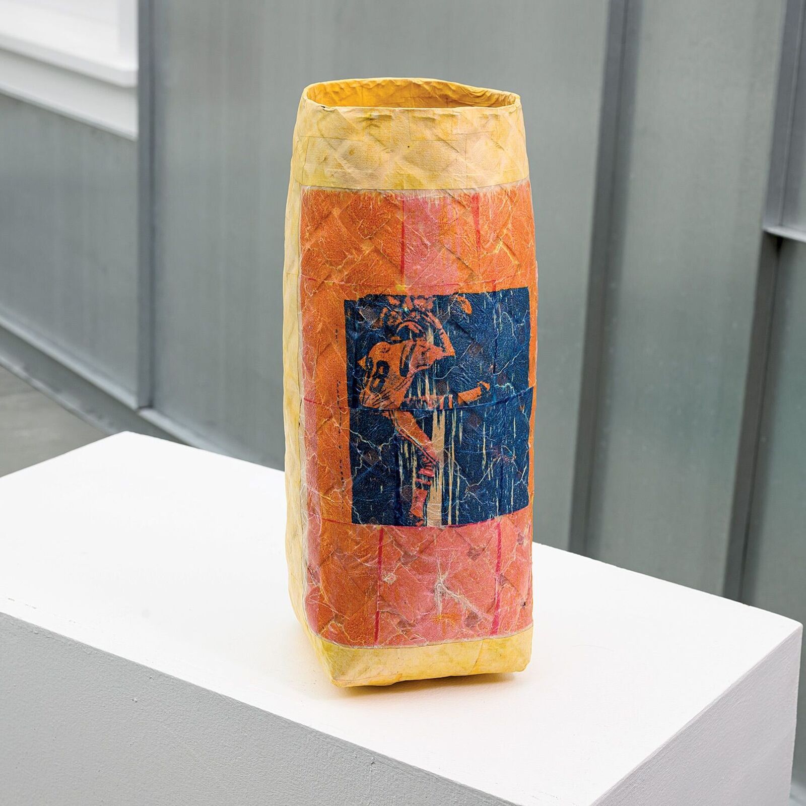 A textured, multi-colored vase featuring a blue square print of a figure.