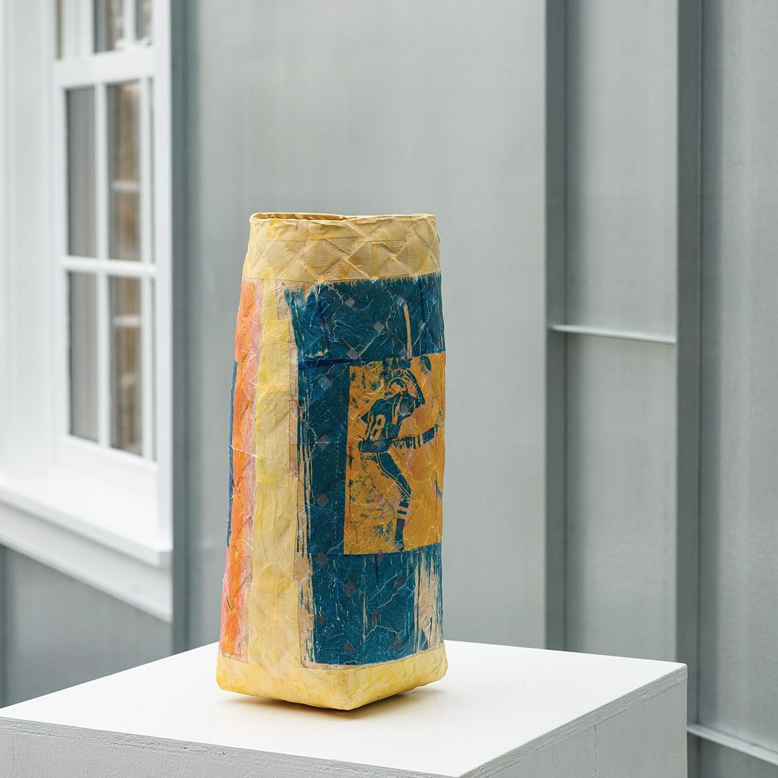 A textured, multi-colored vase featuring a blue square print of a figure.