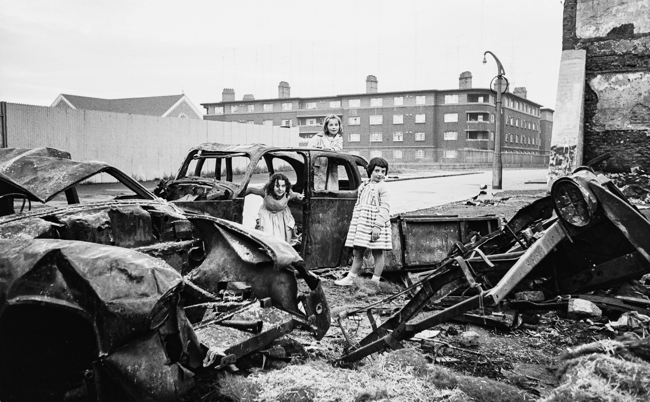 A group of children standing next to a pile of wrecked cars.