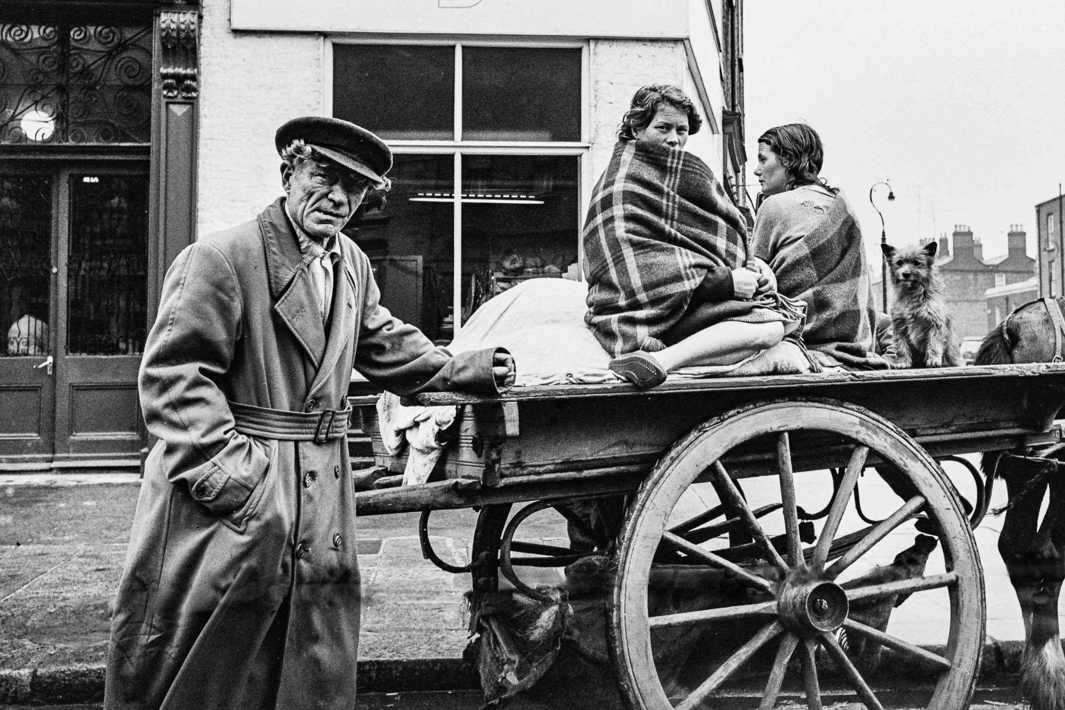 A man standing next to a horse drawn cart with people on it.