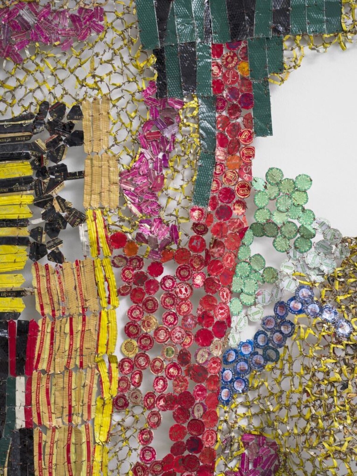 A textured, net-like sculpture featuring a stylized figure and colorful geometric elements against a plain white wall.