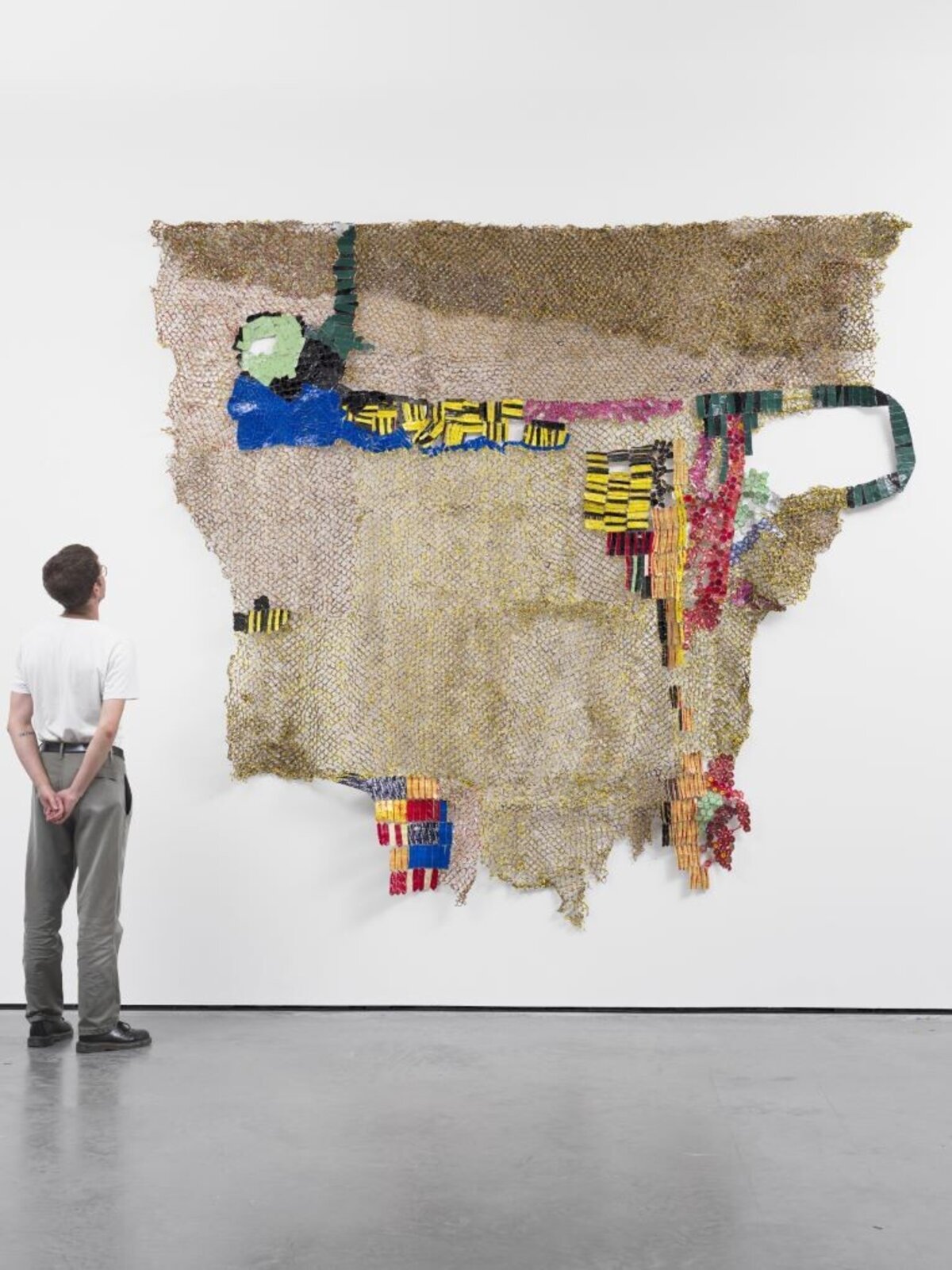 A textured, net-like sculpture featuring a stylized figure and colorful geometric elements against a plain white wall.