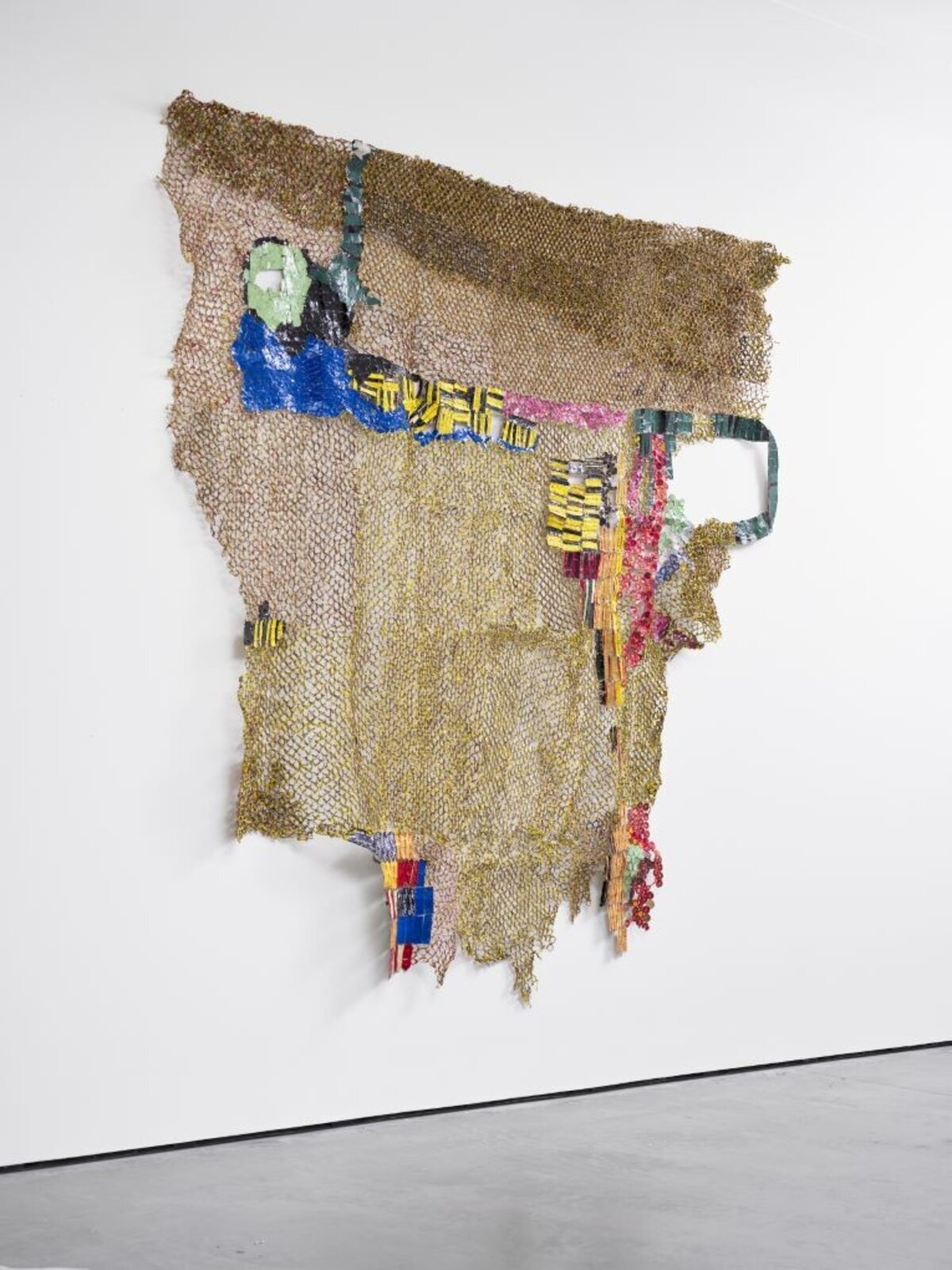 A textured, net-like sculpture featuring a stylized figure and colorful geometric elements against a plain white wall.