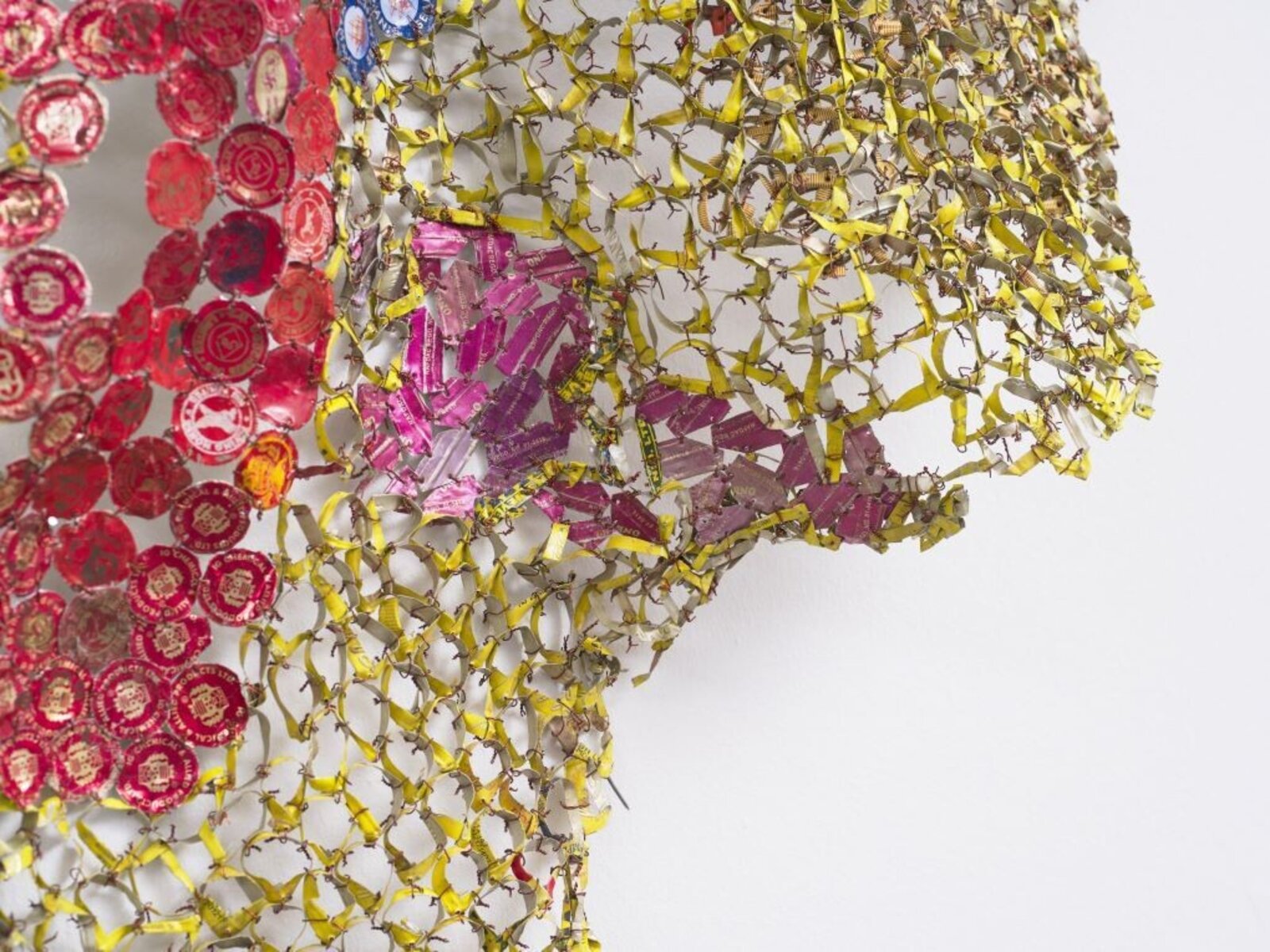A textured, net-like sculpture featuring a stylized figure and colorful geometric elements against a plain white wall.