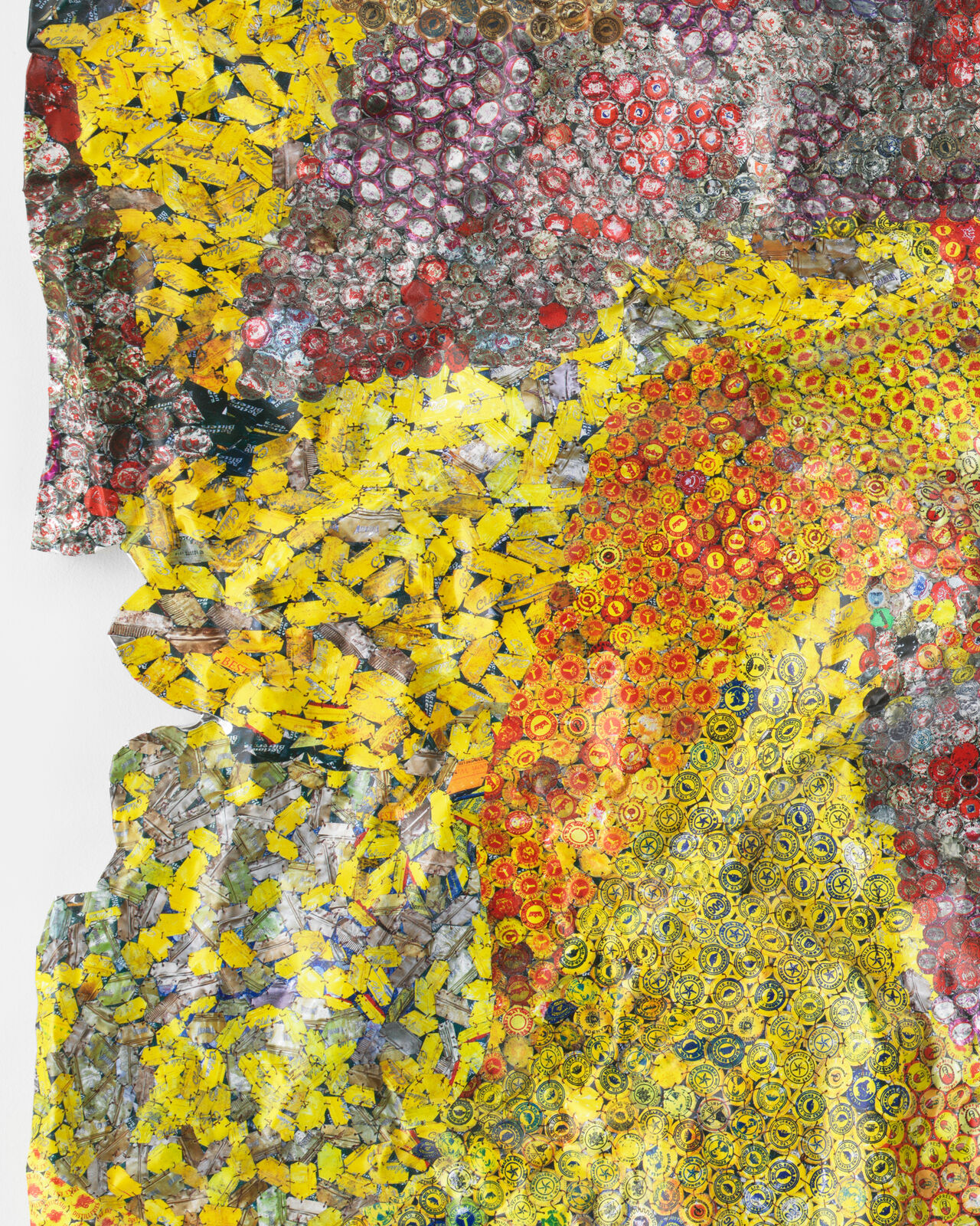 A colorful, crumpled textile-like artwork made from thousands of tiny bottle caps.
