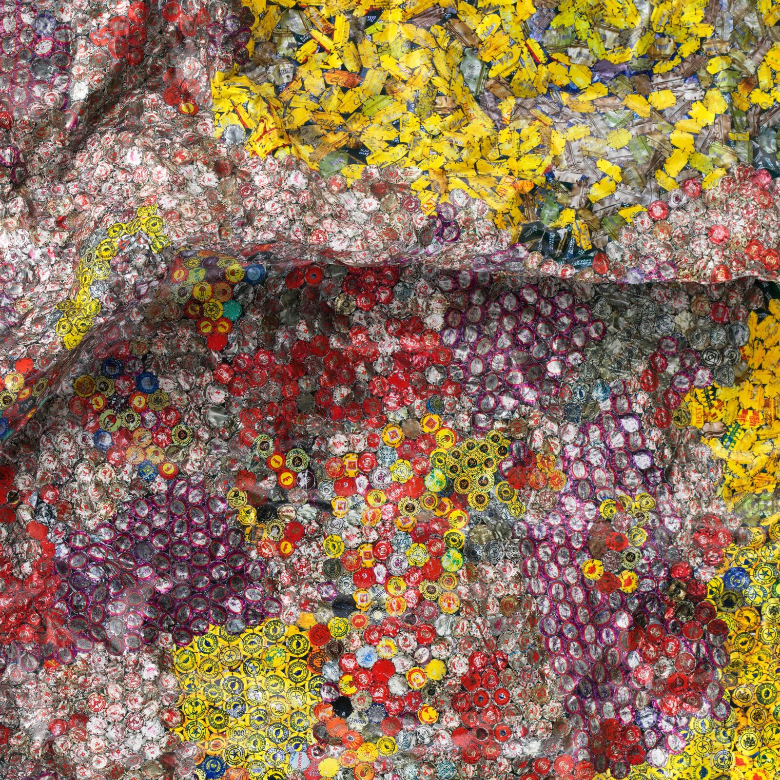 A colorful, crumpled textile-like artwork made from thousands of tiny bottle caps.
