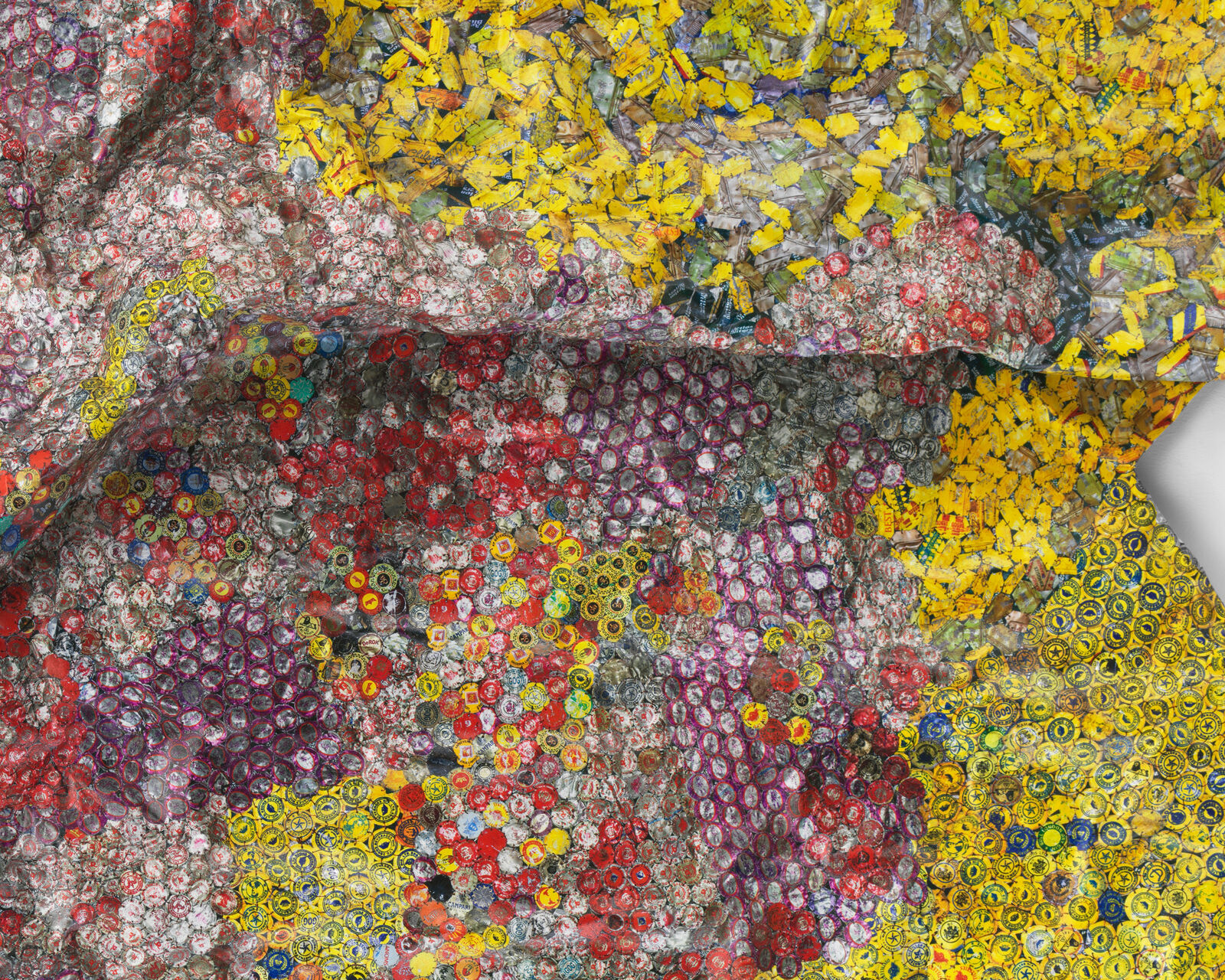 A colorful, crumpled textile-like artwork made from thousands of tiny bottle caps.