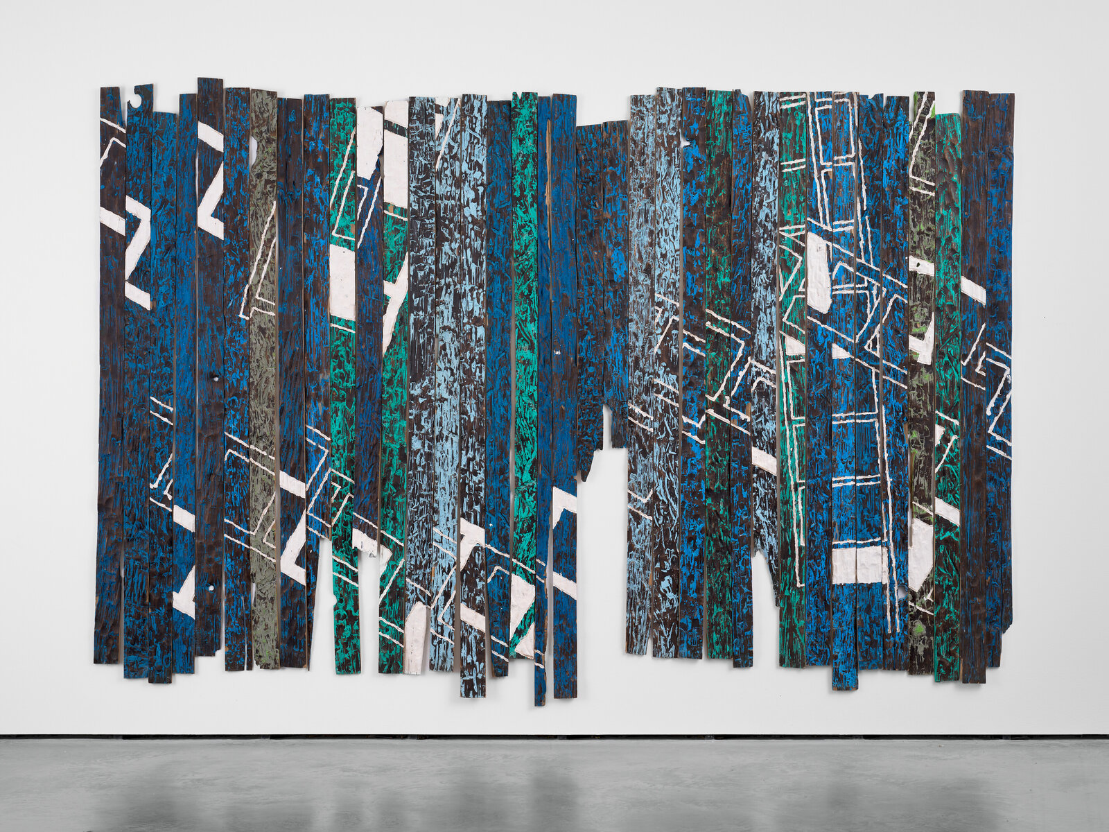 A large-scale mixed media artwork featuring vertical wooden slats painted in bold blues and greens with white geometric markings.