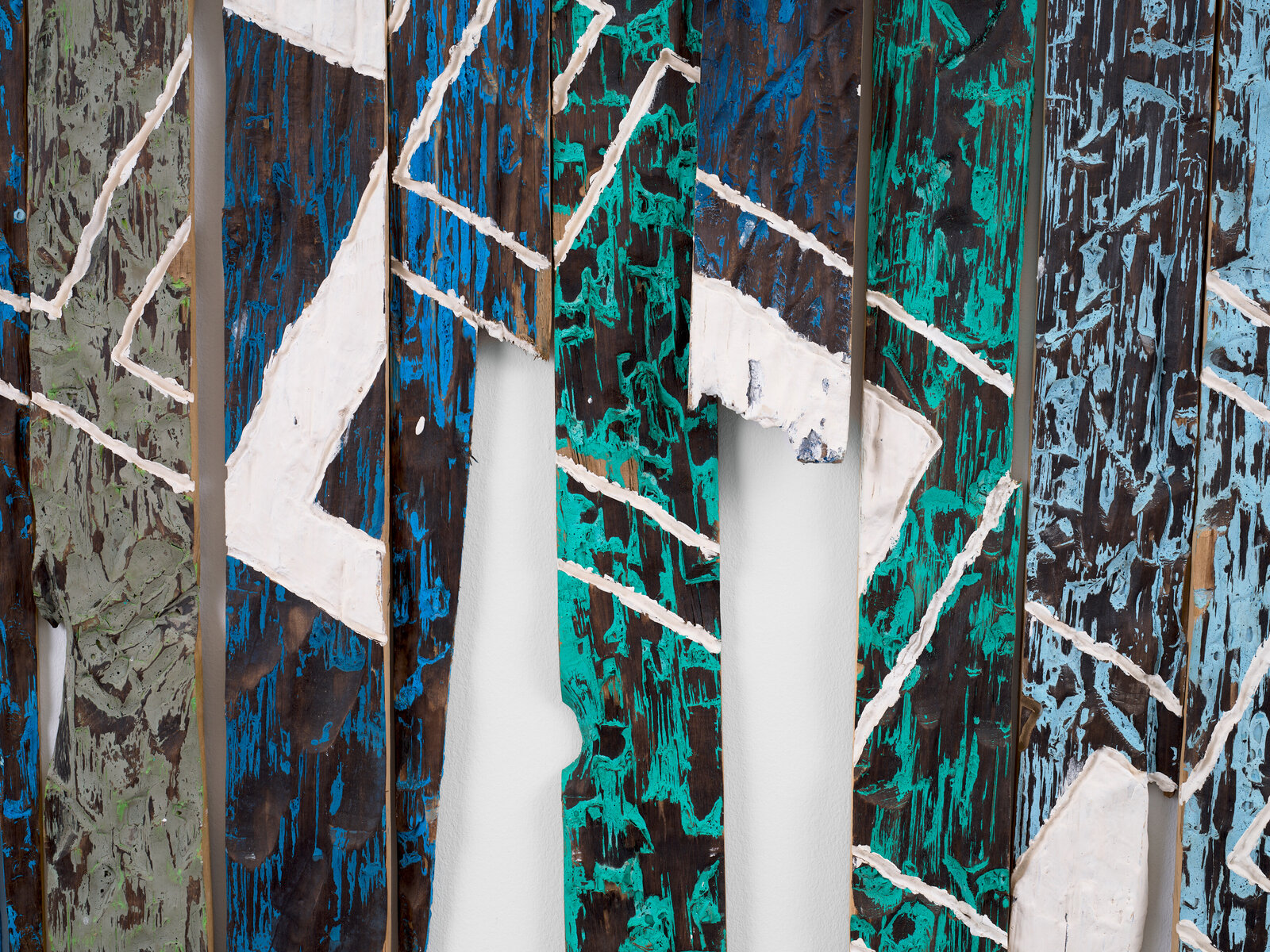 A large-scale mixed media artwork featuring vertical wooden slats painted in bold blues and greens with white geometric markings.