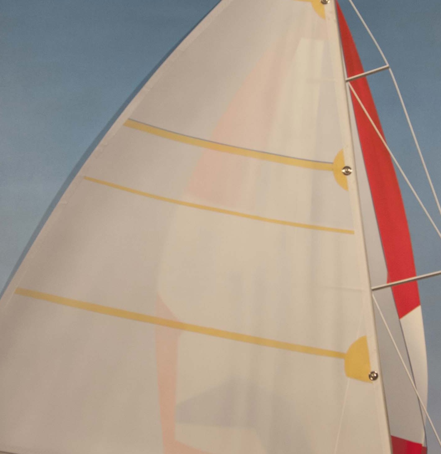 A sailboat with a red and white sail on a blue sky.