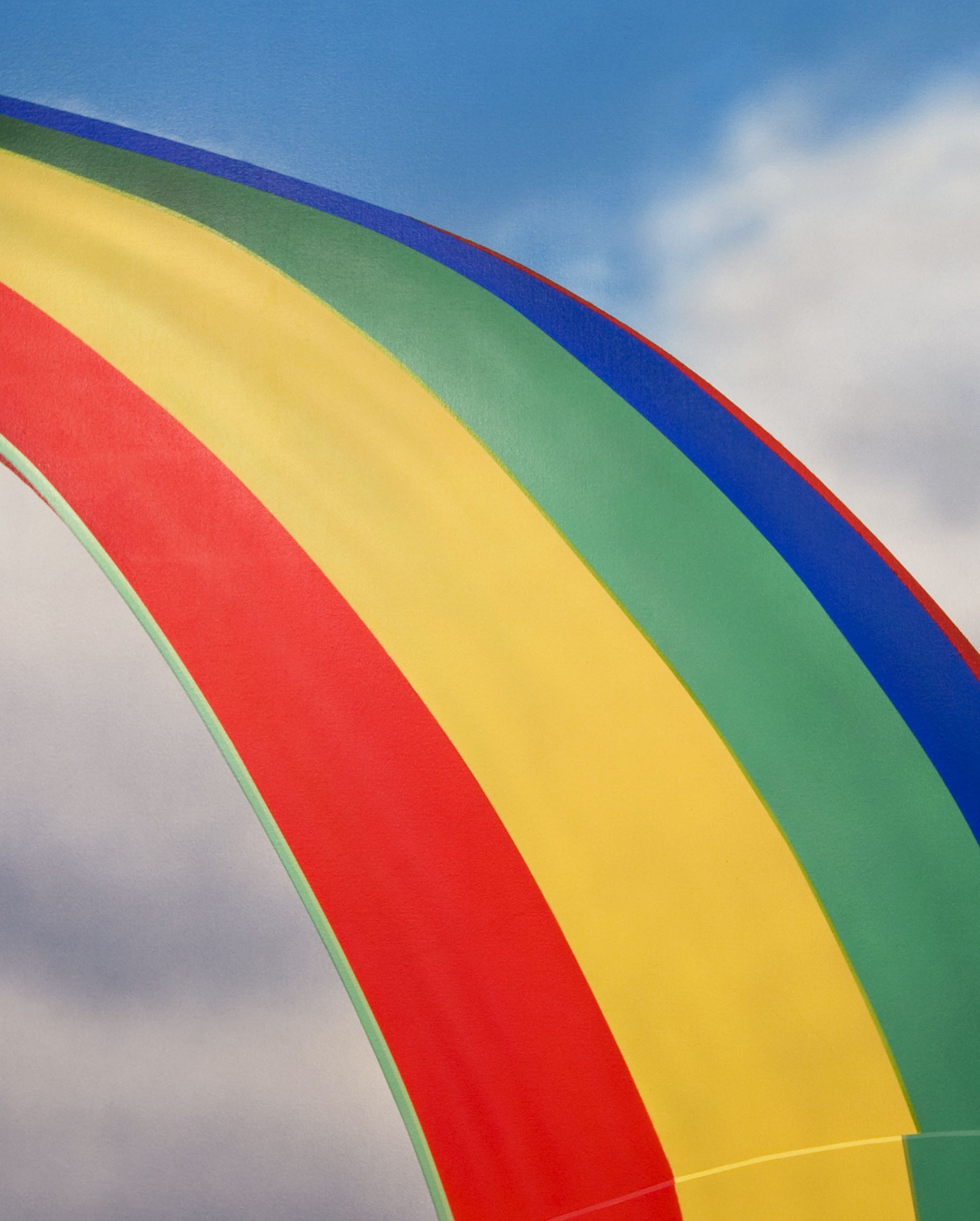 A rainbow colored kite flying in the sky with clouds in the background.