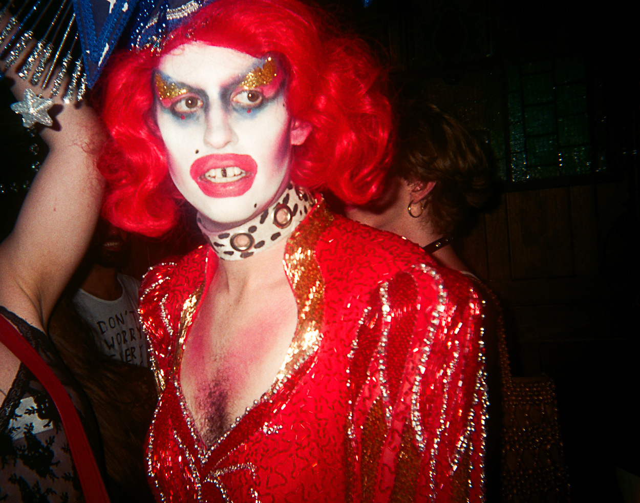 A woman dressed as a clown with red hair and makeup.