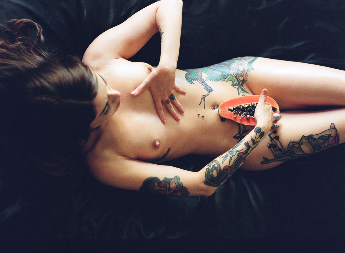 A woman laying on a black couch holding a papaya.