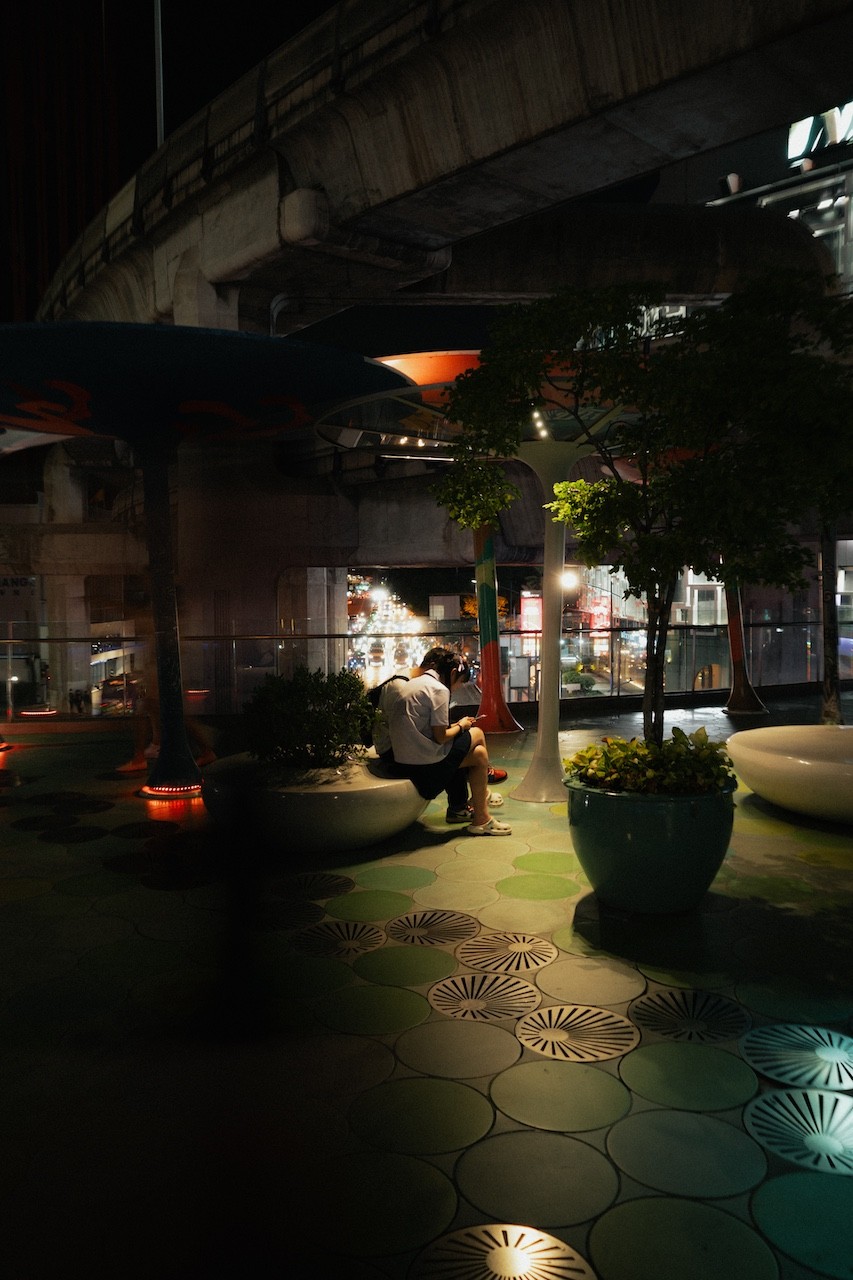 A man sitting on a bench in the middle of a city at night.