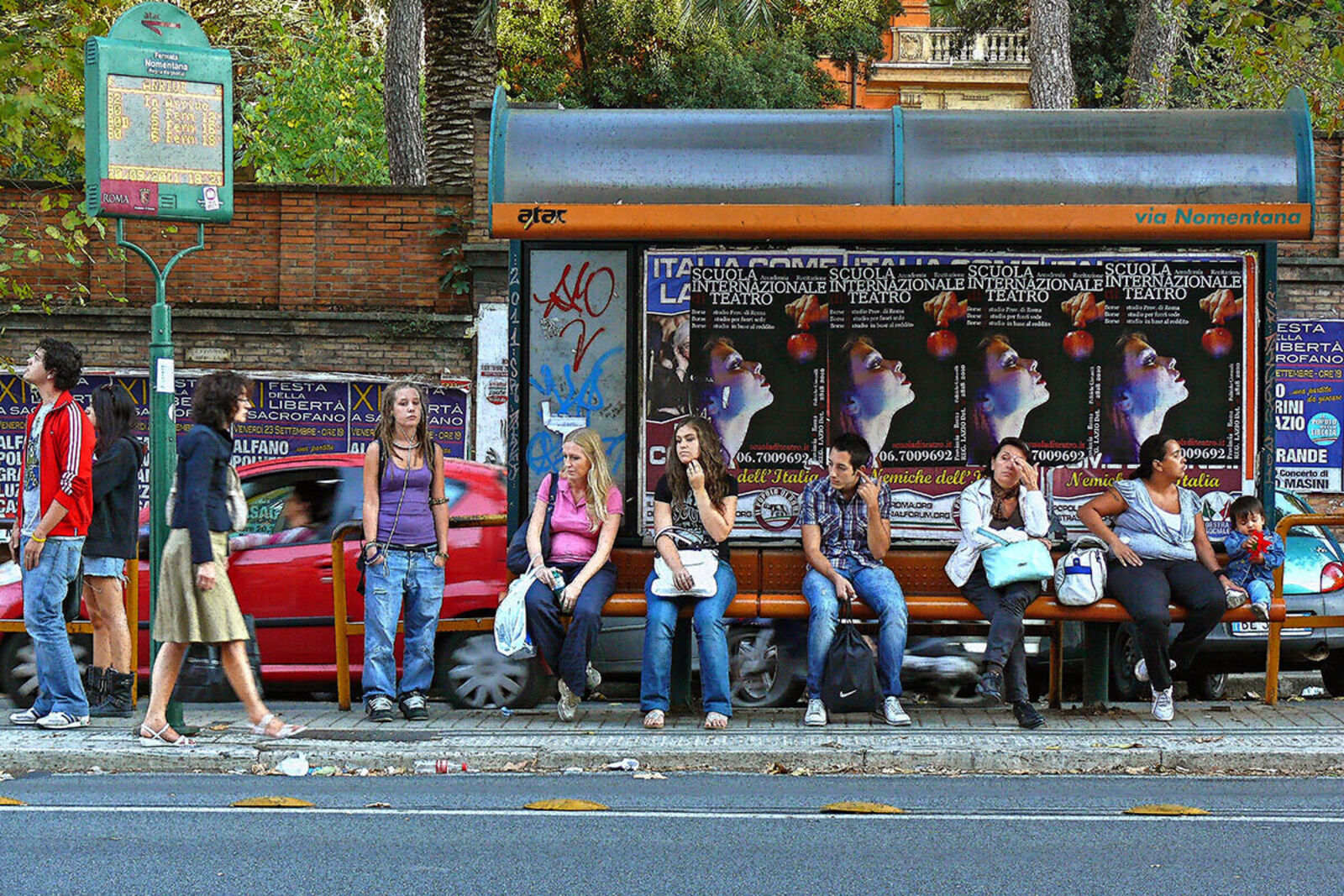 A group of people sitting on a bench in front of a bus stop.